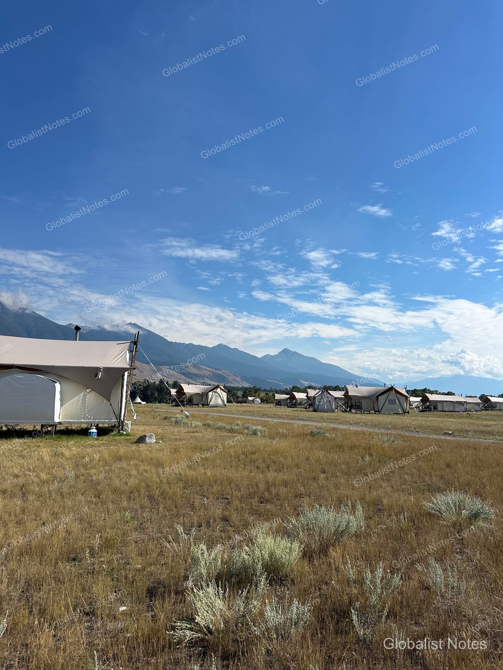 Under Canvas North Yellowstoneの全景。黄金色の草原にデラックステントやキッズテントが点在し、背後には雄大な山脈がそびえています。