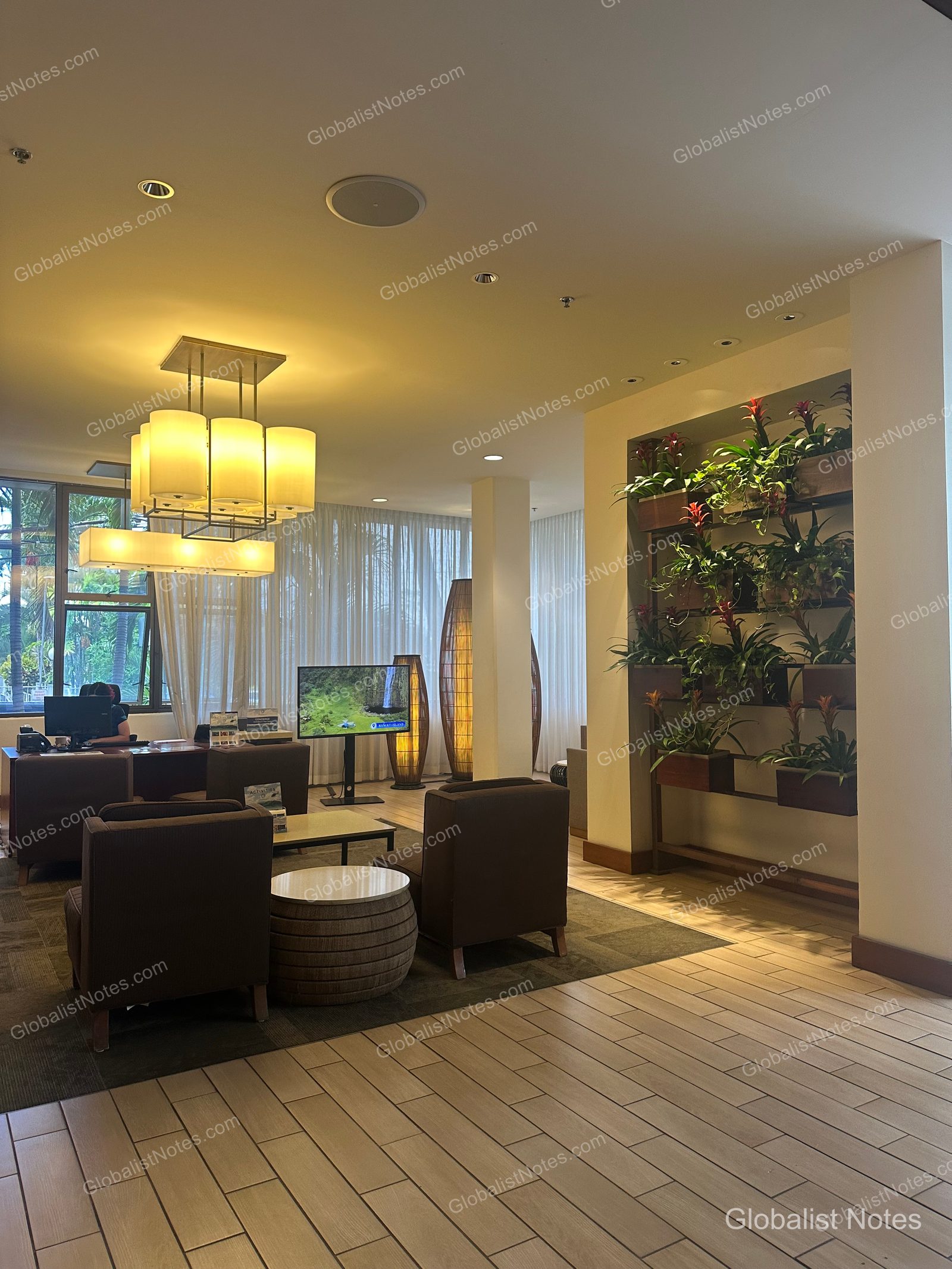 Lobby area at Hyatt Place Waikiki Beach in Honolulu, featuring brown armchairs, round tables, a vertical garden wall, and rectangular ceiling lighting.