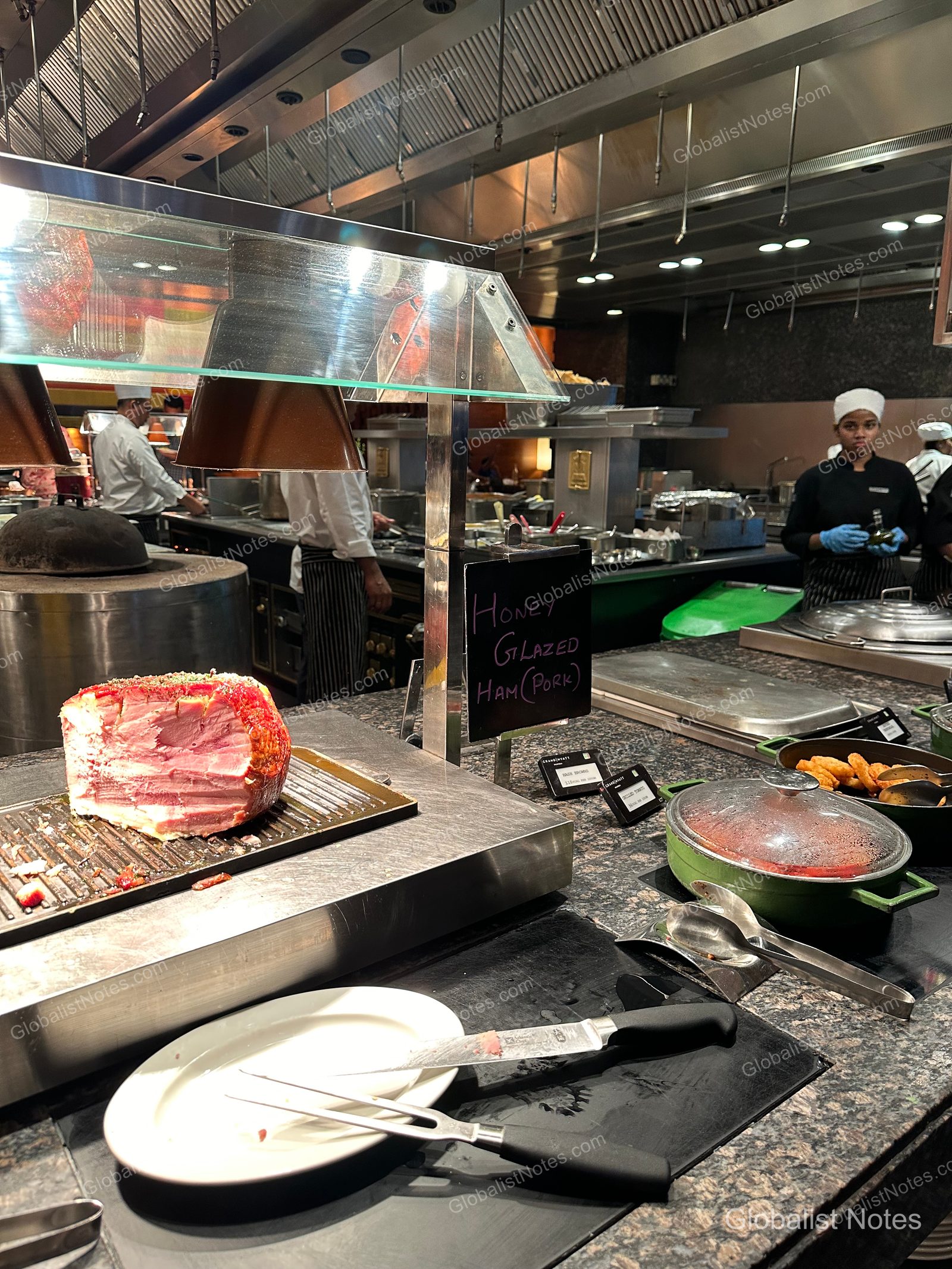 A live cooking station at the Grand Hyatt Mumbai breakfast buffet, featuring honey-glazed ham under warm lighting with chefs working in the background.