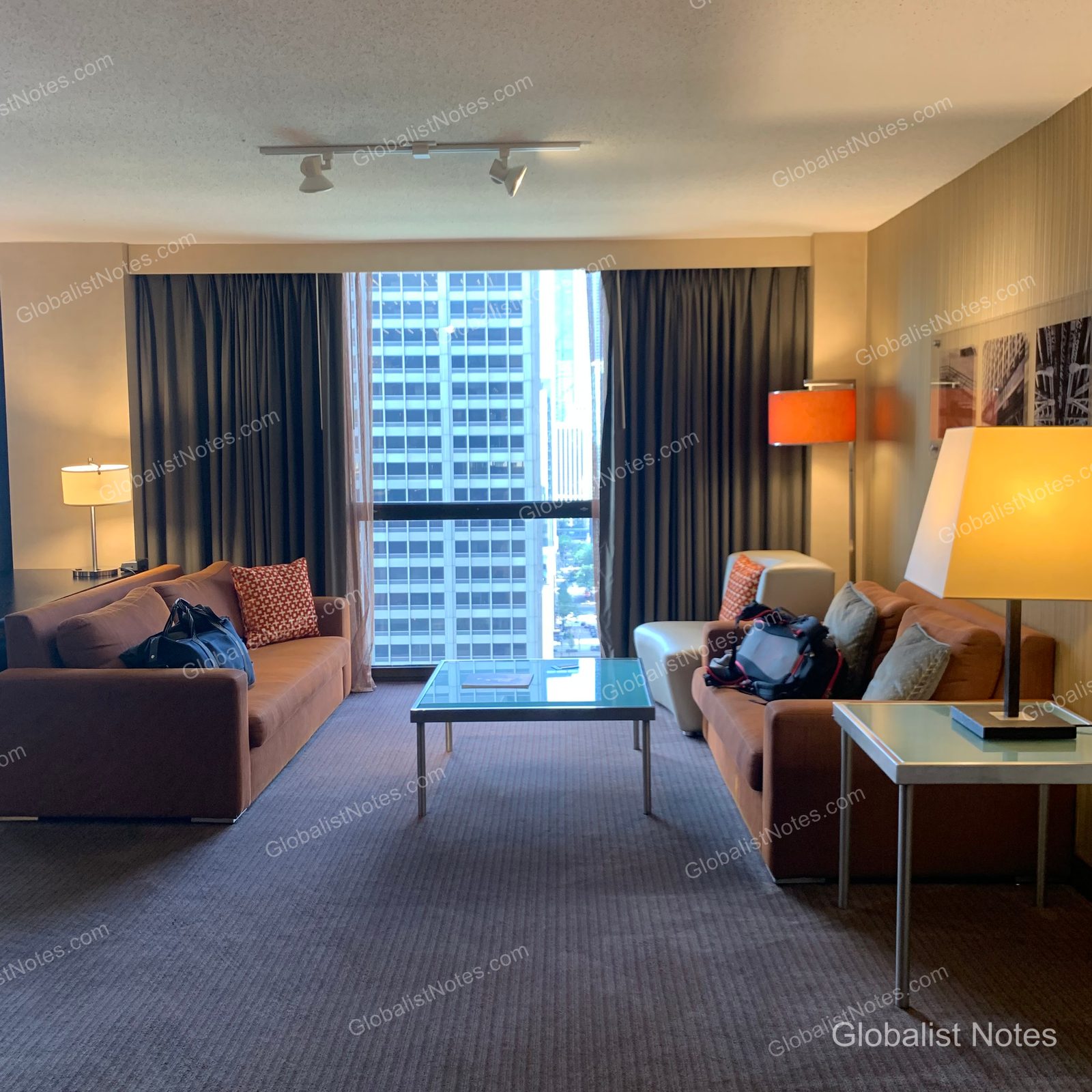 Hyatt Regency Chicagoのジュニアスイートのリビングエリア。向かい合わせに配置されたブラウンのソファと中央のガラステーブル、そしてシカゴのビル群を望む大きな窓が特徴的。