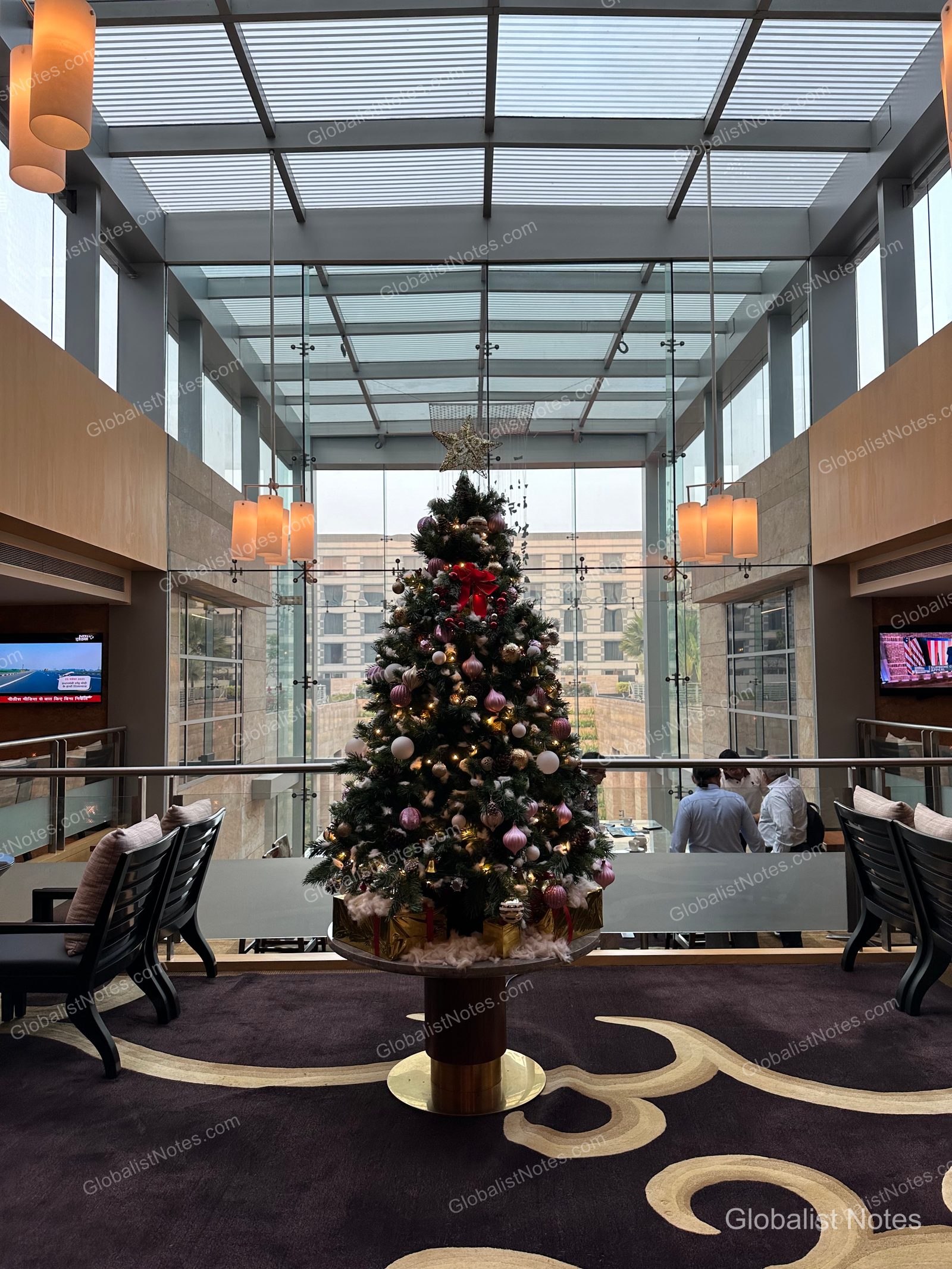 A large Christmas tree in the center of the Grand Hyatt Mumbai lounge, bathed in natural light from the high glass ceiling and surrounded by seating areas.
