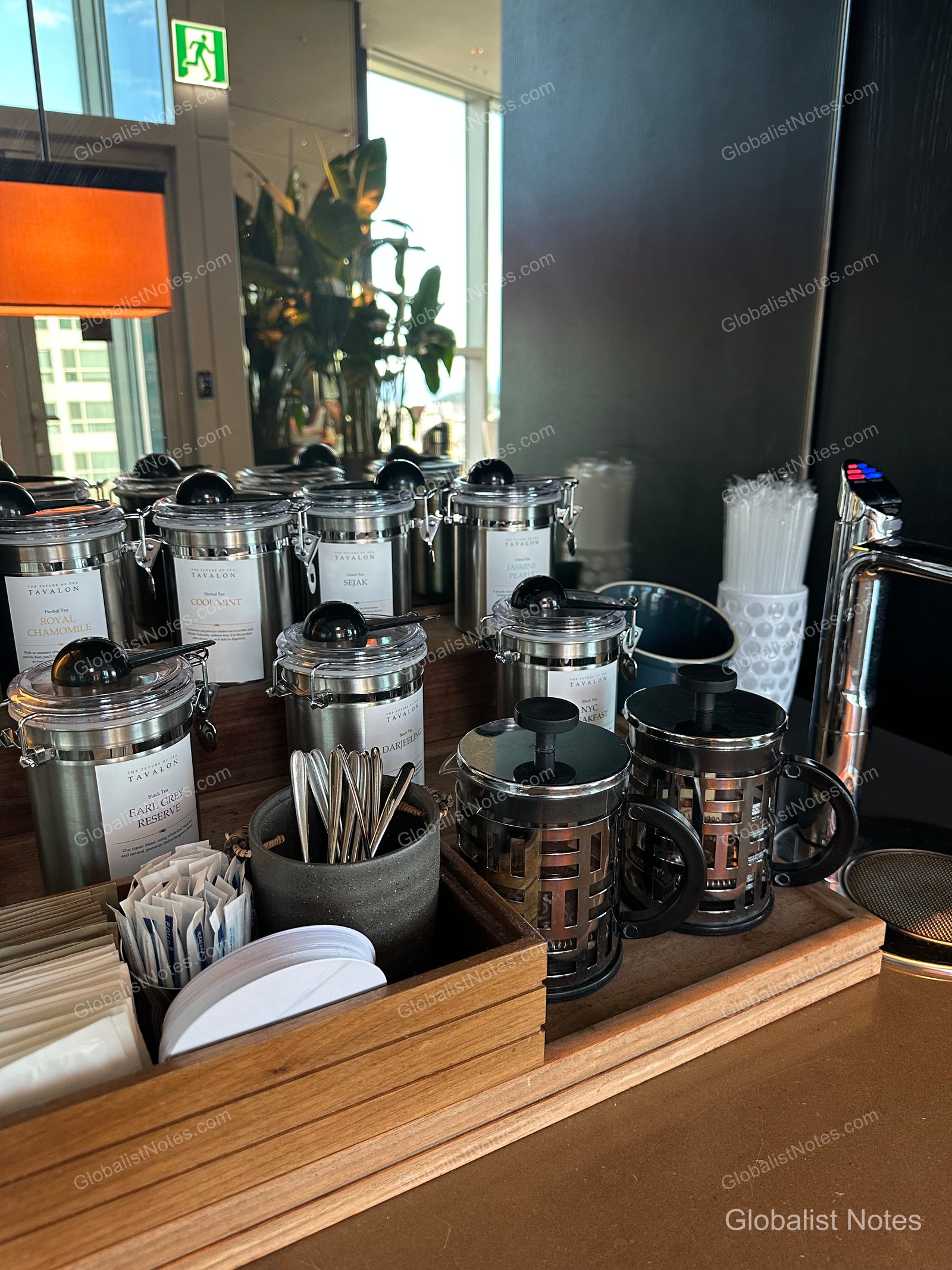 Silver airtight canisters from the Tavalon tea collection, a French press, stick sugar, and teaspoons neatly arranged on a wooden tray in the Grand Hyatt Jeju lounge.