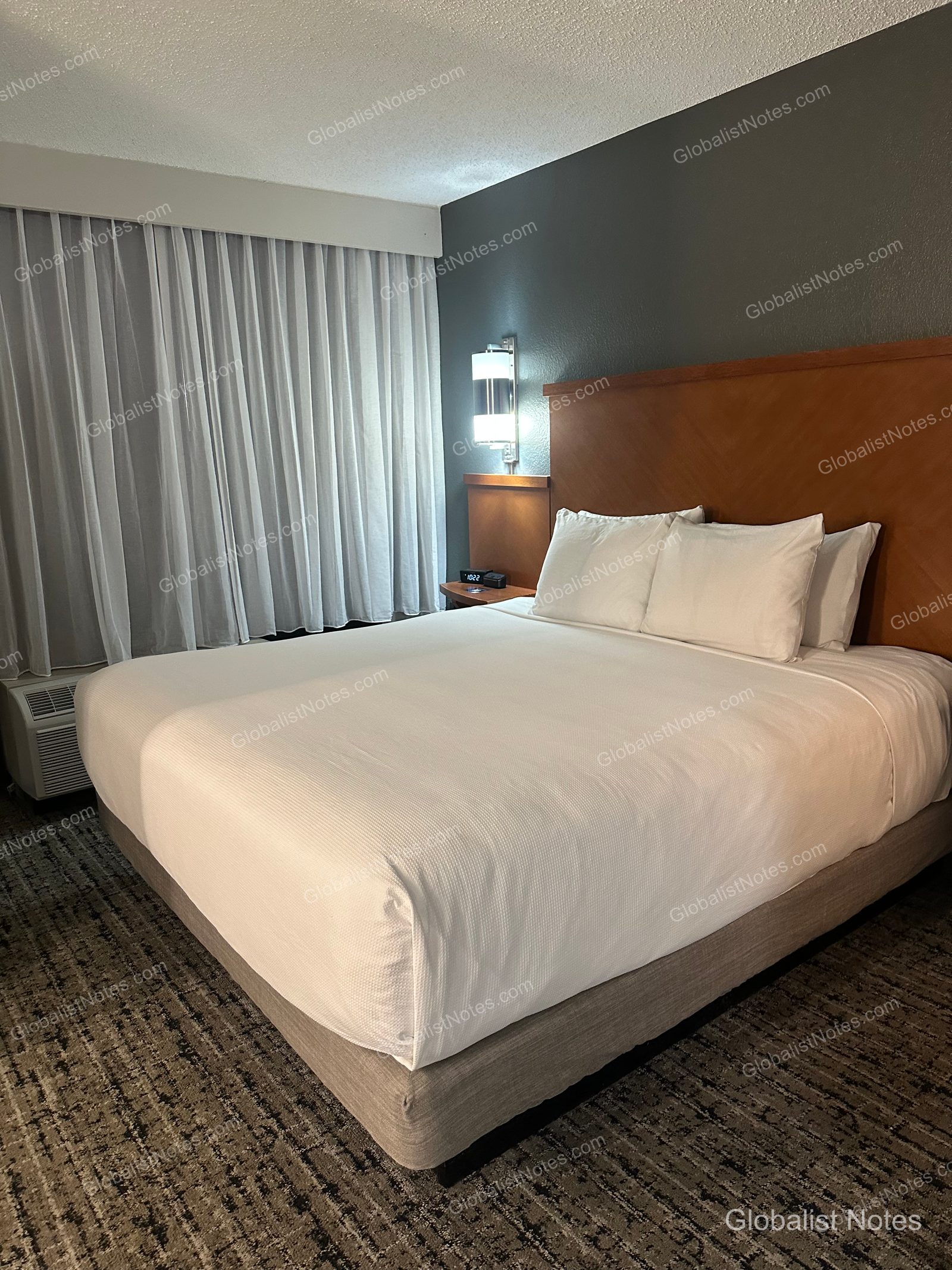 Hyatt Place El Paso Airport 的 Junior Suite 內部。中央擺放一張配有木質床頭板的特大雙人床，背景為深灰色牆面，左側可見帶有白色窗簾的窗戶與空調設備。