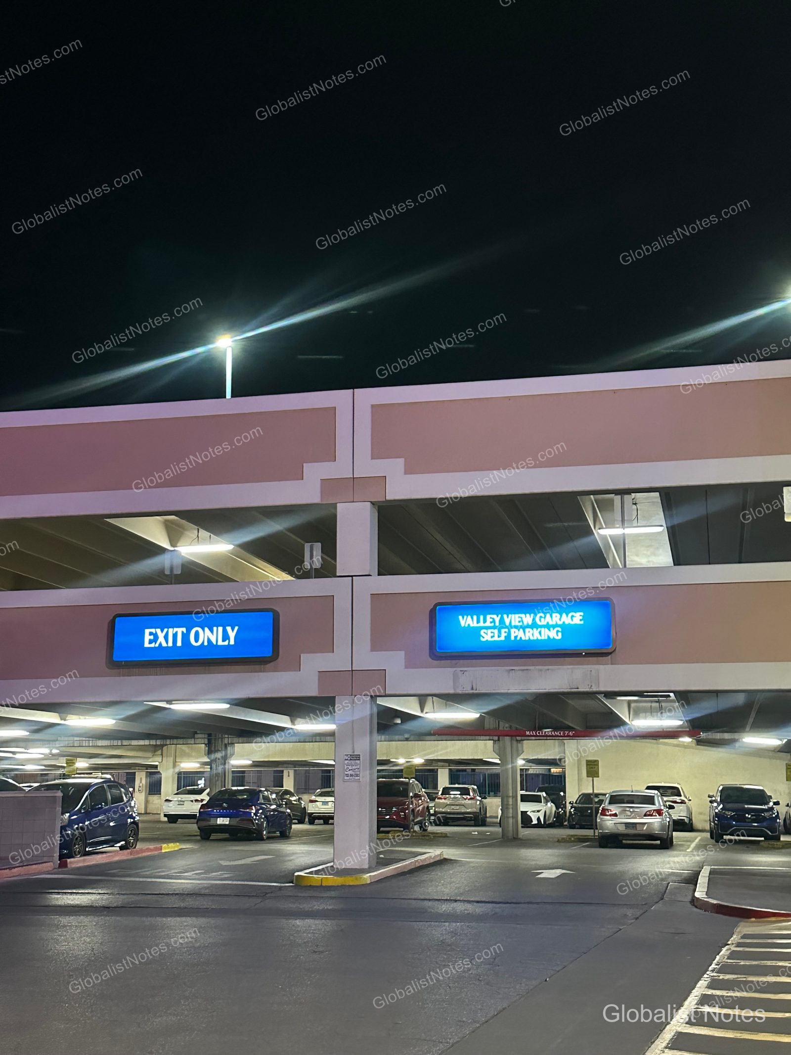 라스베이거스 리오 호텔 앤 카지노의 야간 주차장 입구 모습입니다. 'EXIT ONLY'와 'VALLEY VIEW GARAGE SELF PARKING'이라고 적힌 파란색 조명 표지판이 기둥 위에 설치되어 있고, 아래층 주차 구역에는 여러 대의 차량이 주차되어 있습니다.