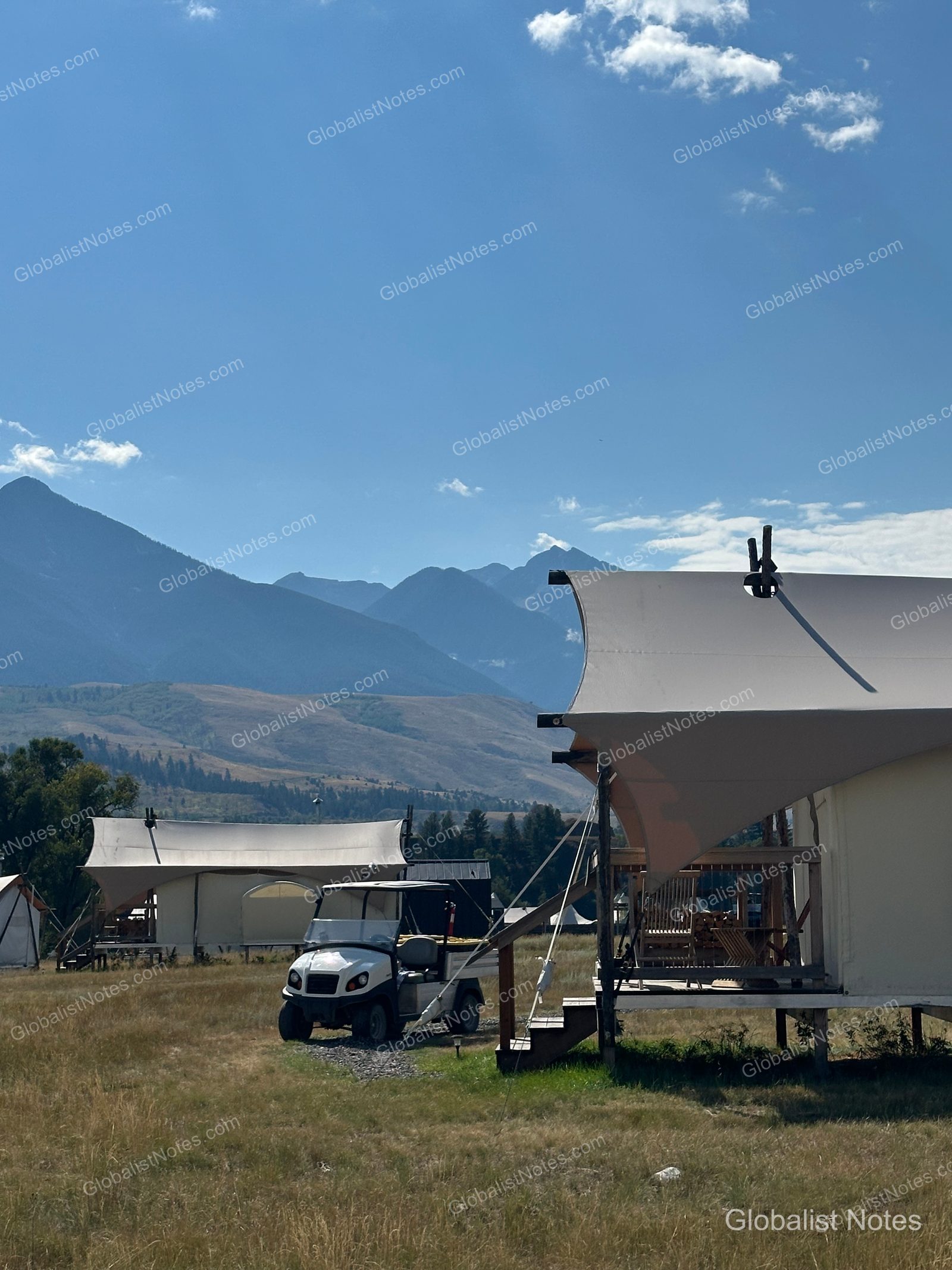 Under Canvas North Yellowstone - Paradise Valleyのジュニアスイートテント。広大な草原にテントが並び、横には移動用のゴルフカートが停まっている。背景には雄大な山脈が広がる。