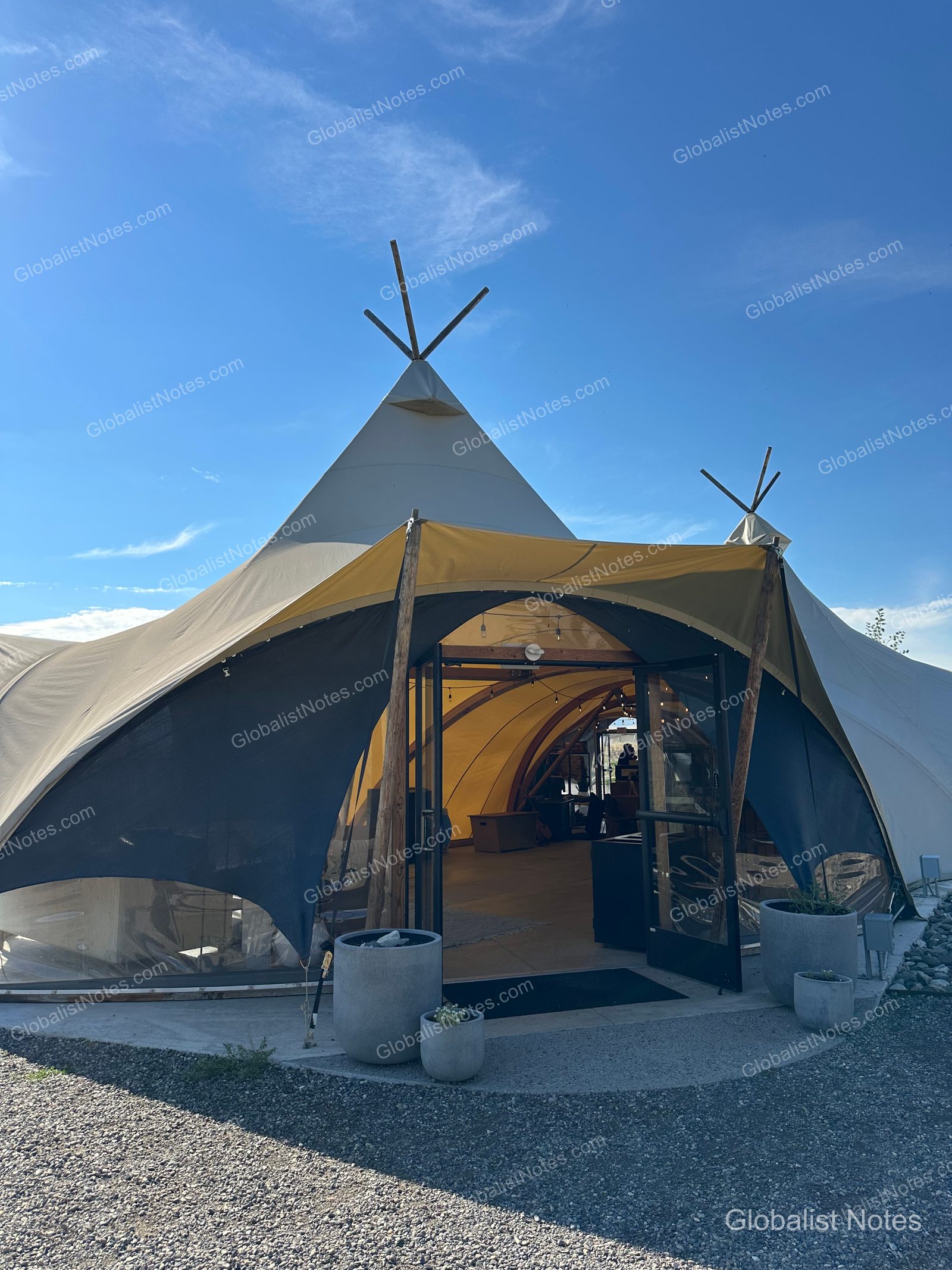 Under Canvas North Yellowstoneのロビーテント入り口。ベージュのキャンバス地に覆われた円錐形の構造物の前に植木鉢が置かれ、開かれたガラス扉から内部が見える。