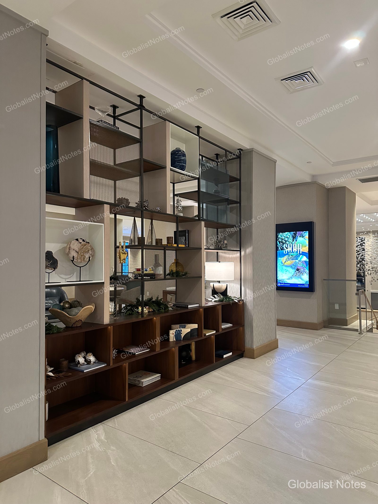 Hyatt Regency La Jolla at Aventine 大廳，牆面設有金屬框架與木質層架組成的大型裝飾櫃，擺放各式擺飾與燈具，側邊牆面則有數位看板。