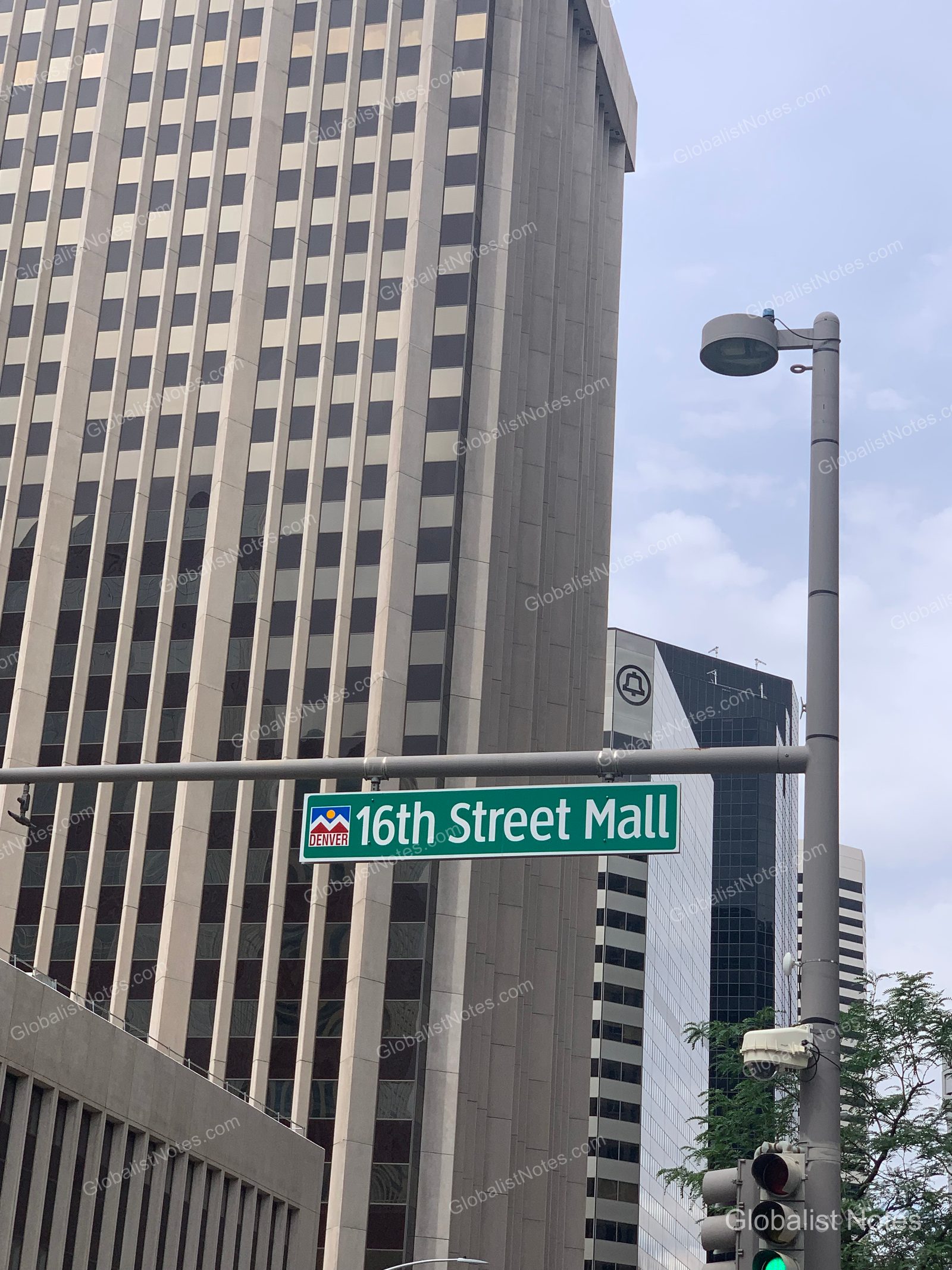 デンバーのダウンタウン、高層ビルが立ち並ぶ16th Street Mallの緑色の道路標識。手前には信号機と街灯が写っている。