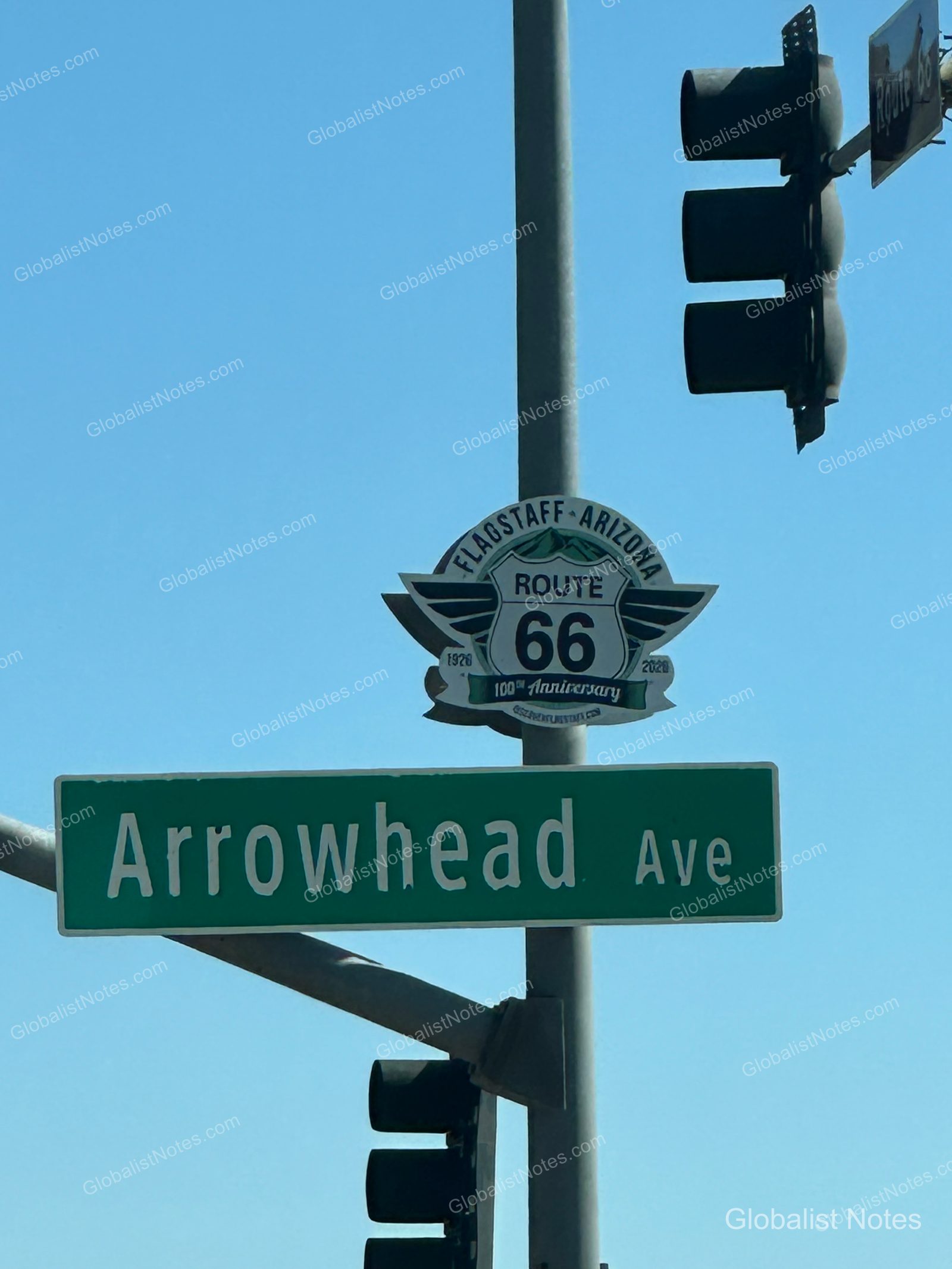 米国アリゾナ州フラッグスタッフの青空を背景に、信号機の支柱に取り付けられたArrowhead Aveの道路標識とルート66の100周年記念標識。