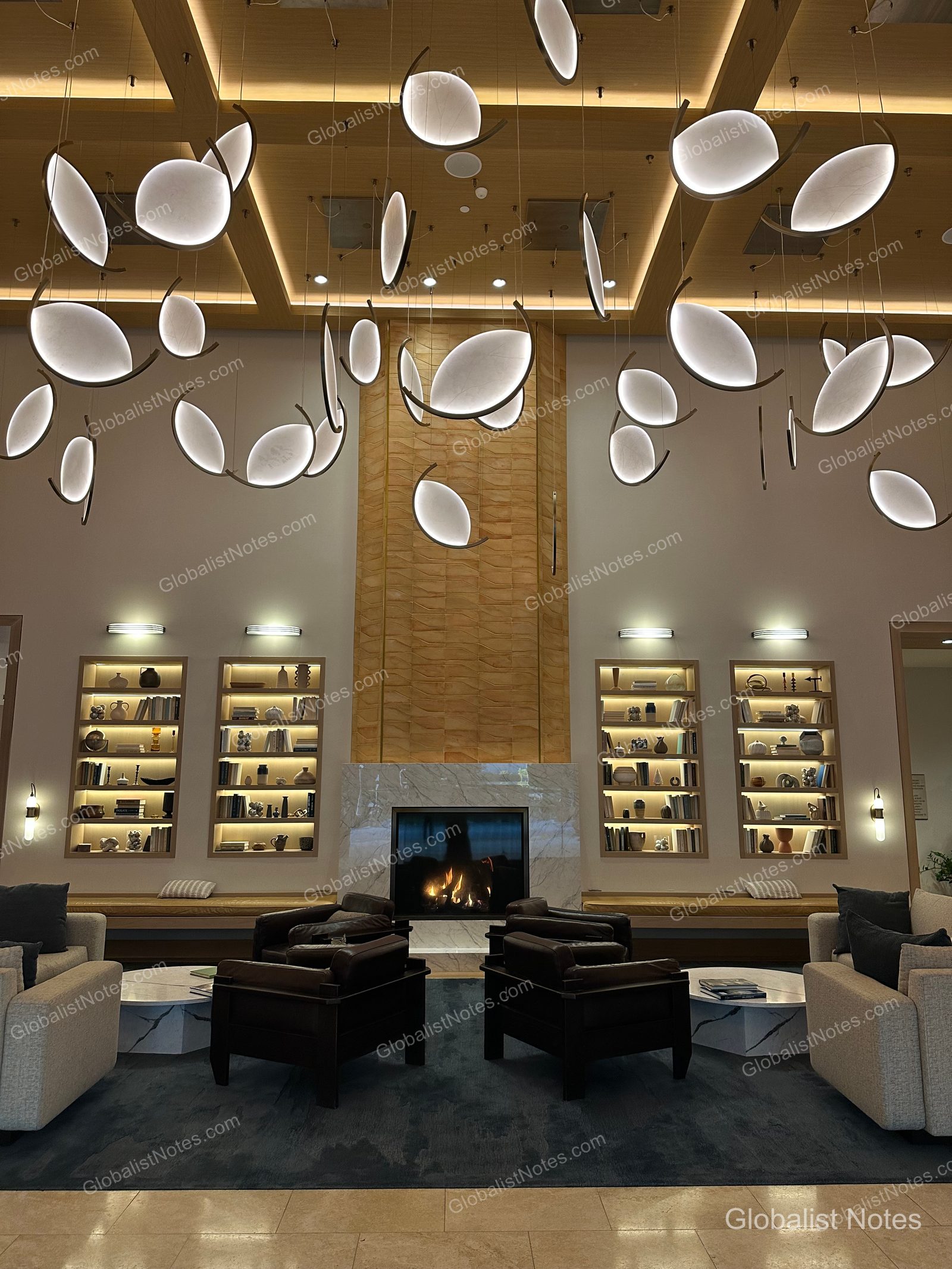 Hyatt Regency Irvine 大廳中央的壁爐，上方懸掛葉片造型燈飾。前方設有對稱的書架、皮革扶手椅及大理石桌休憩區。