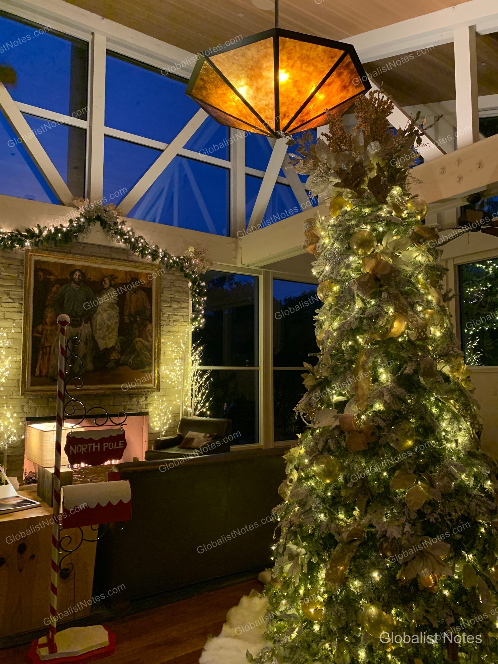 Carmel Valley Ranchのロビーに飾られた大きなクリスマスツリーと「North Pole」の看板。高いガラス窓からは夕暮れ時の空が見え、暖炉上の絵画と温かみのある照明が空間を照らしている。