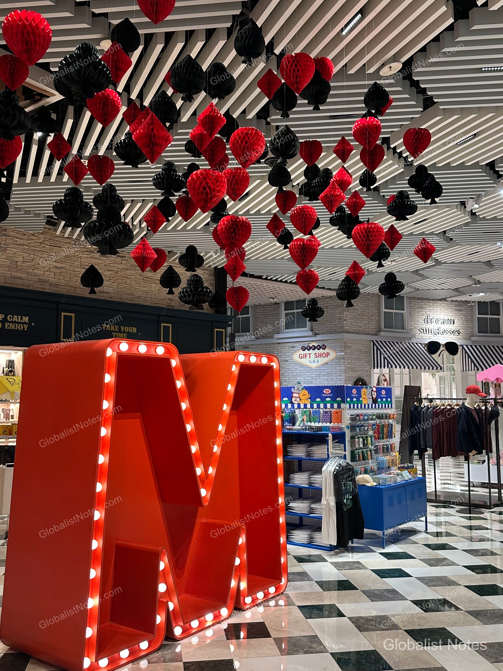 A large red 'M' sculpture and numerous red and black heart-shaped decorations hanging from the ceiling inside the Grand Hyatt Jeju shopping mall.