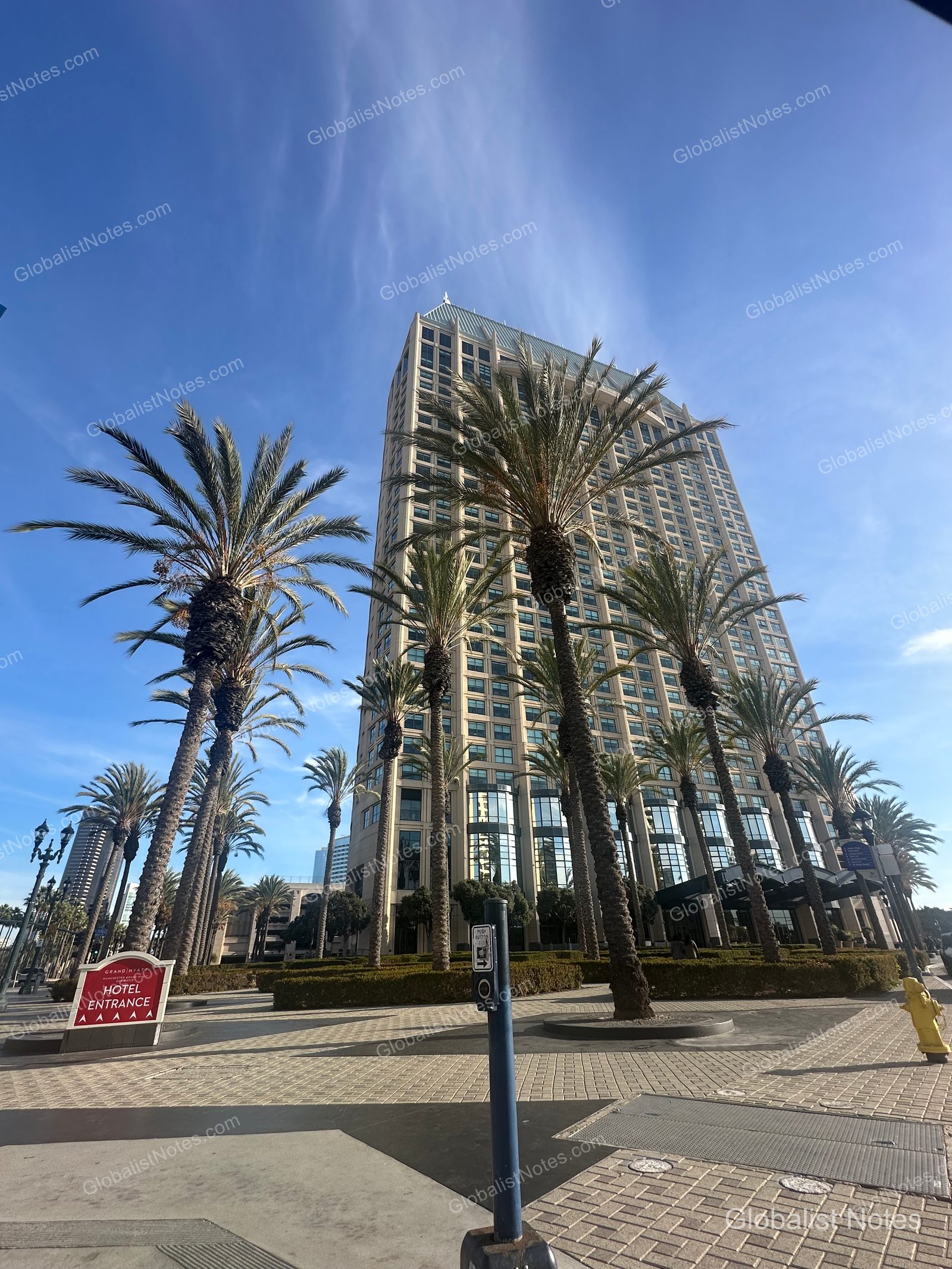 Manchester Grand Hyatt San Diego 外觀。高樓前方排列著棕櫚樹，左側立有飯店入口招牌，背景為晴朗藍天。