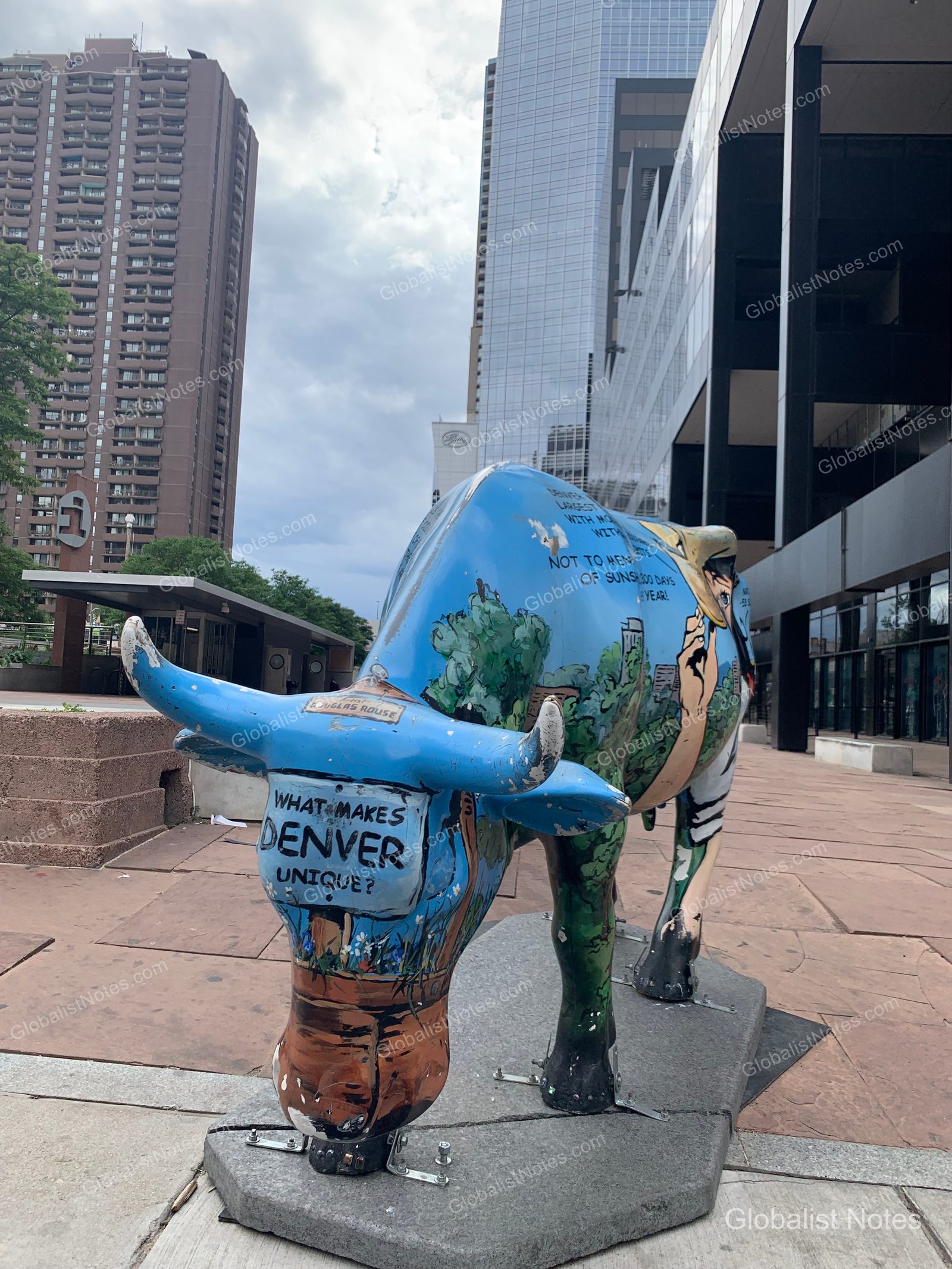 Grand Hyatt Denver近くの歩道に置かれた青い牛のオブジェ。体にはデンバーの街並みを描いたイラストや文字が施され、背景には高層ビルが並ぶ。