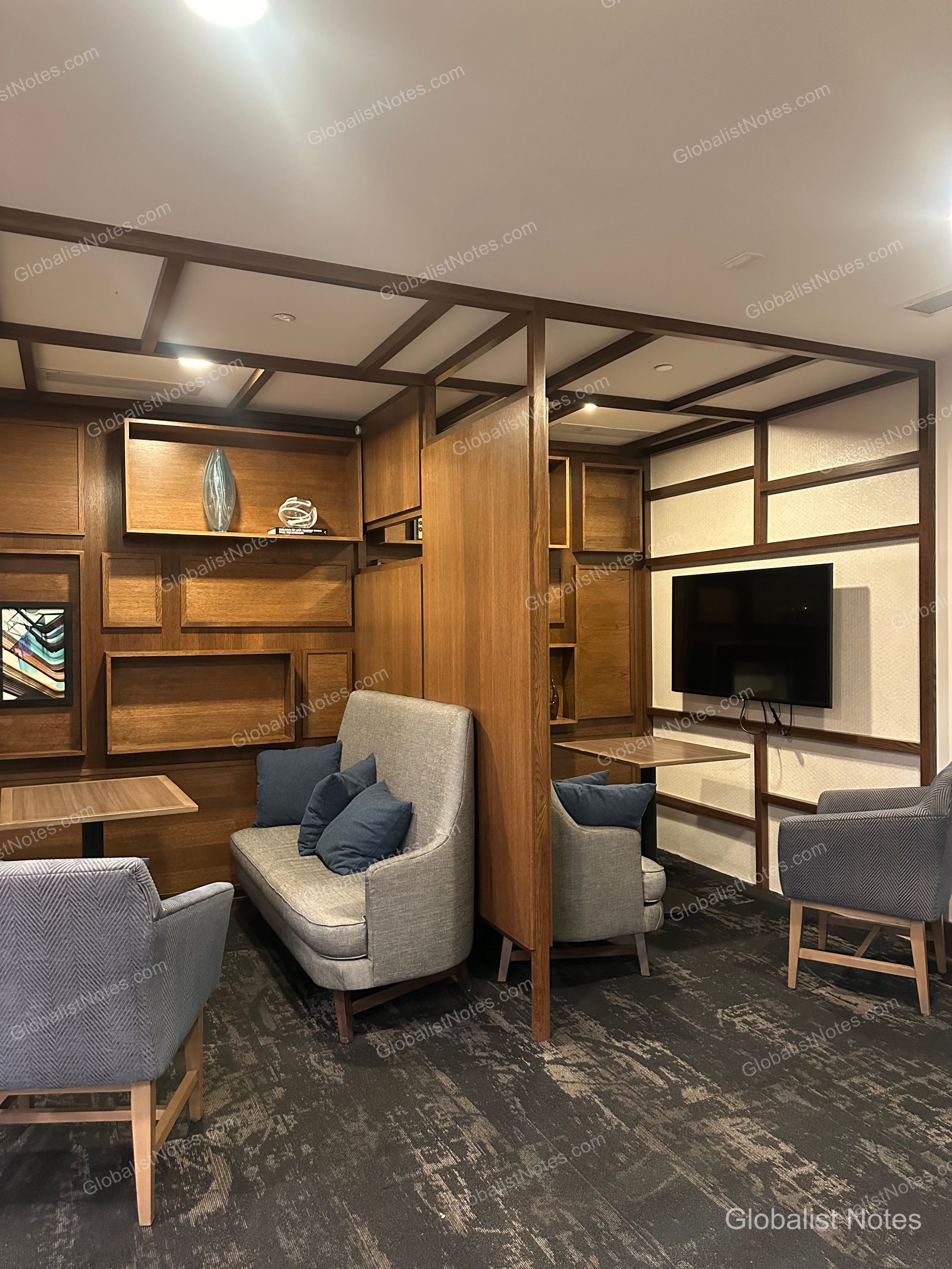 Hyatt Place Tucson-Central 大廳休息區，設有木質格柵牆面、灰色沙發與單人椅。空間透過木質隔板劃分，牆面裝飾著層架與壁掛電視。