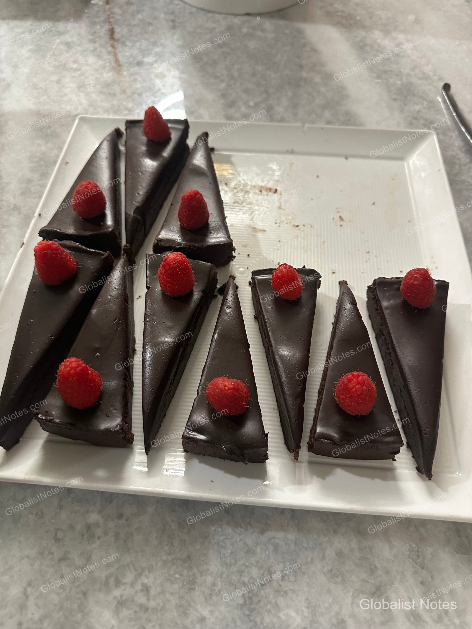 Triangular slices of chocolate cake, each topped with a single raspberry, arranged neatly on white square plates.