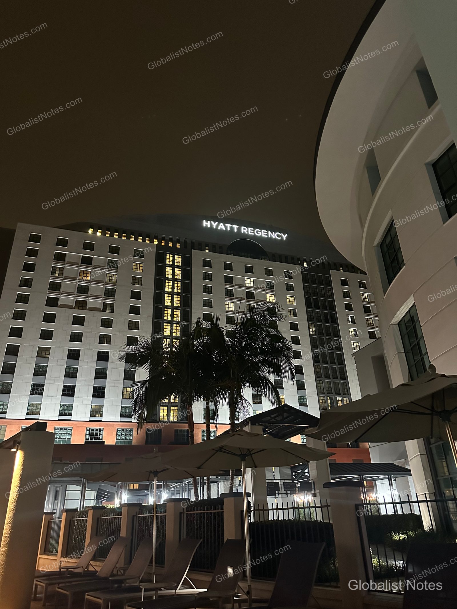 San Diego Hyatt Regency La Jolla at Aventine 飯店夜景，包含打著燈光的高樓外觀、前方的棕櫚樹，以及泳池區的遮陽傘與躺椅。