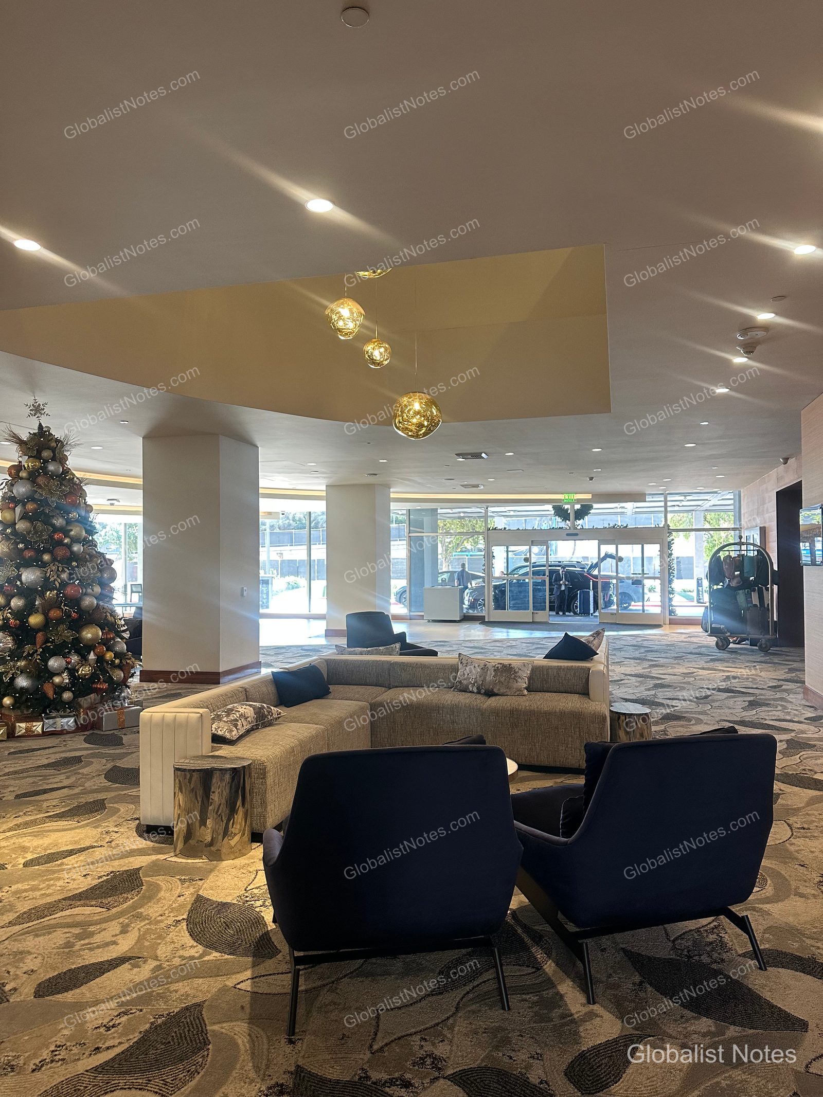 Spacious lobby view at Hyatt Regency Los Angeles International Airport, featuring a Christmas tree, modern seating, and floor-to-ceiling windows overlooking the airport entrance and traffic.