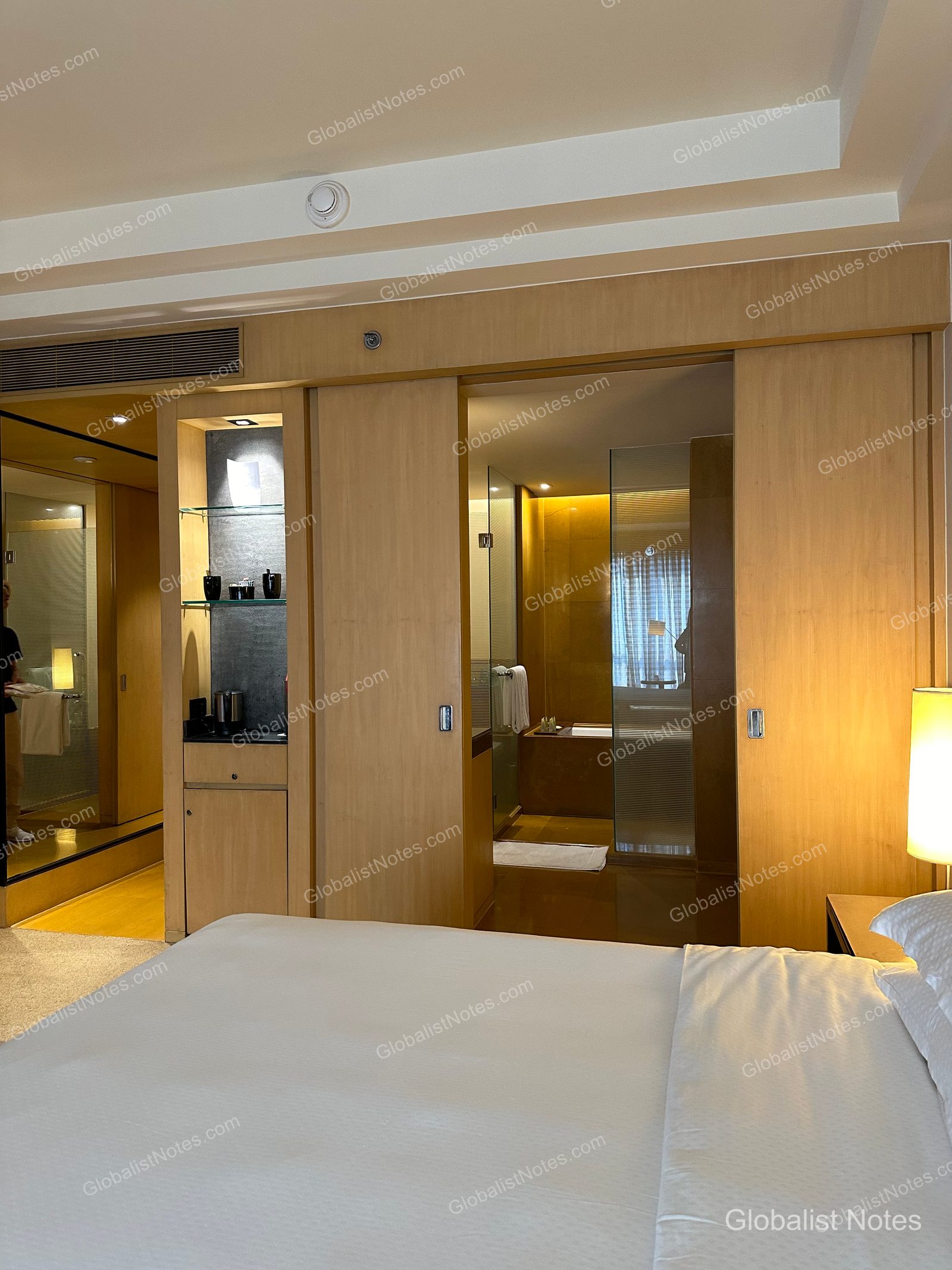 Interior of the Veranda Suite King at Grand Hyatt Mumbai. The sliding door beside the bed is open to the bathroom, with an illuminated minibar and storage unit nearby. The room features warm wood tones and ambient lighting.