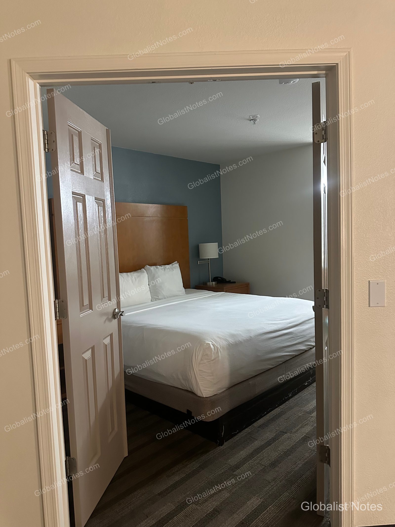 Hyatt House Scottsdale Old Townの1ベッドルームスイート。ドアの向こうに、木製のヘッドボードと青いアクセントウォールが特徴的なベッドルームが見える。