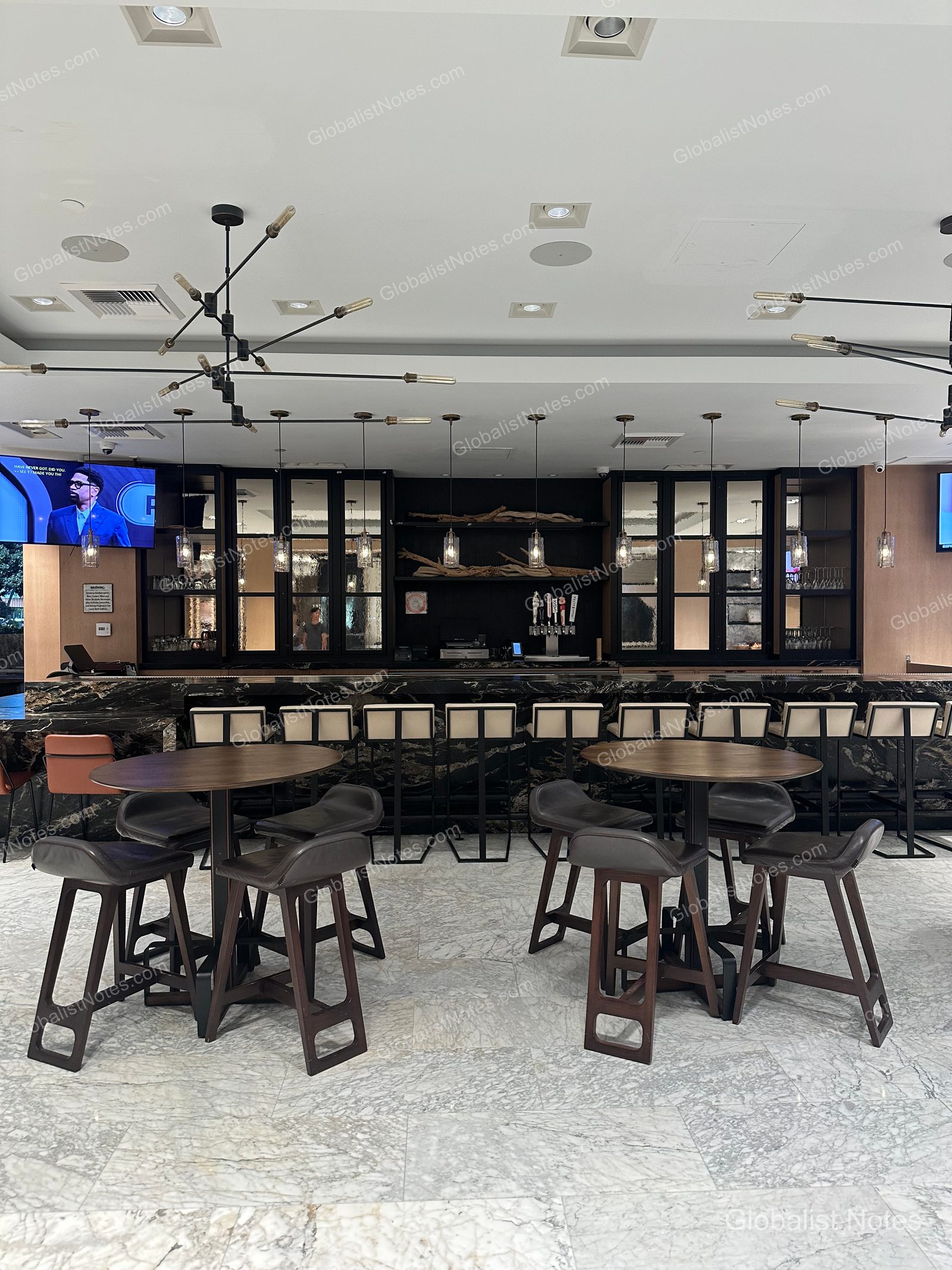 Hyatt Regency Newport Beach 飯店酒吧區，設有黑色大理石吧台與高腳椅。天花板懸掛現代風格燈具，牆面設有玻璃展示櫃與電視，地面鋪設淺色大理石磁磚。