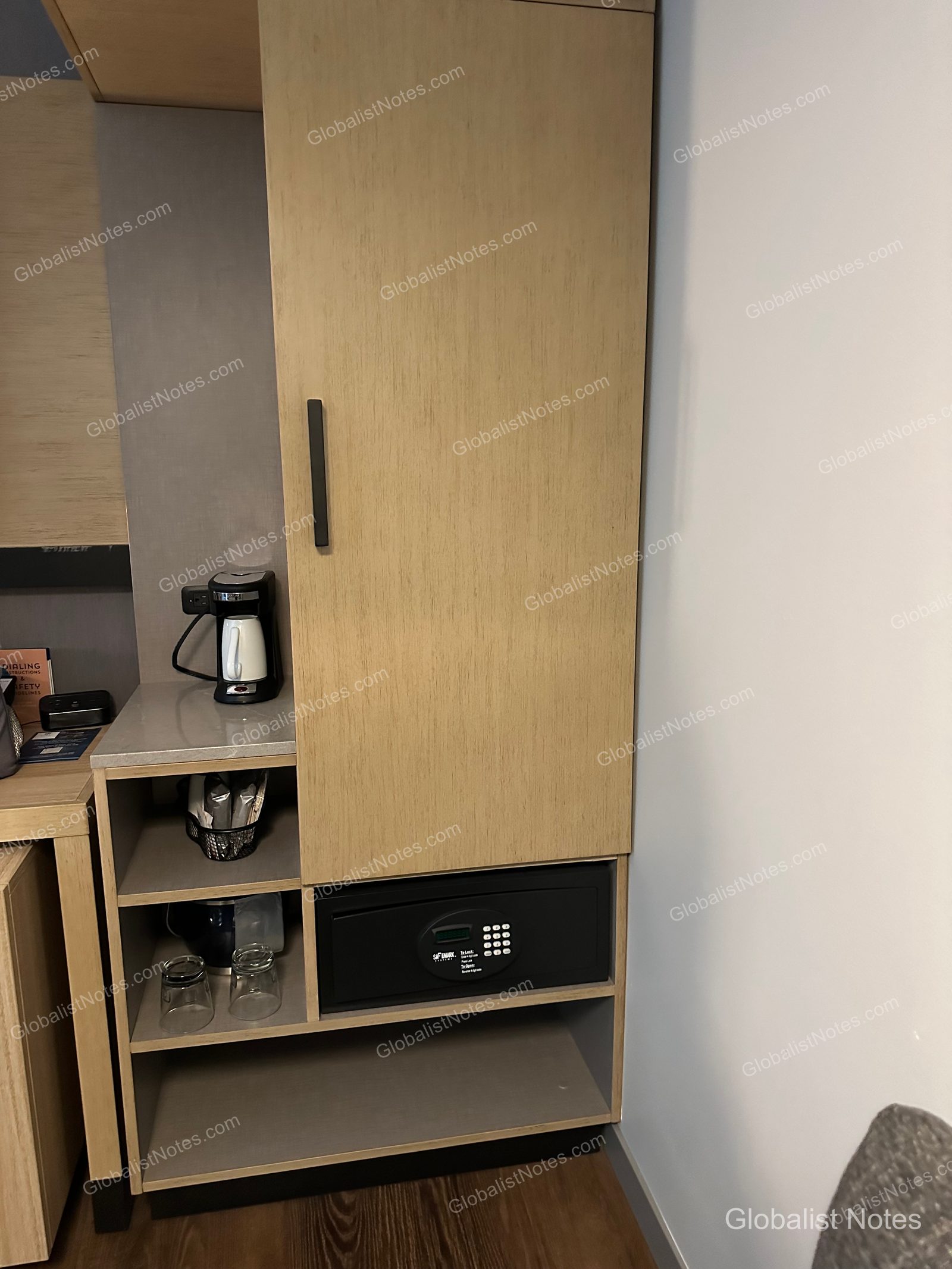 Hyatt Place Bozeman Yellowstone Airportのジュニアスイートにあるミニバーエリア。明るい木目調の棚にコーヒーマシンが置かれ、下のオープンシェルフにはグラスと金庫が収められています。