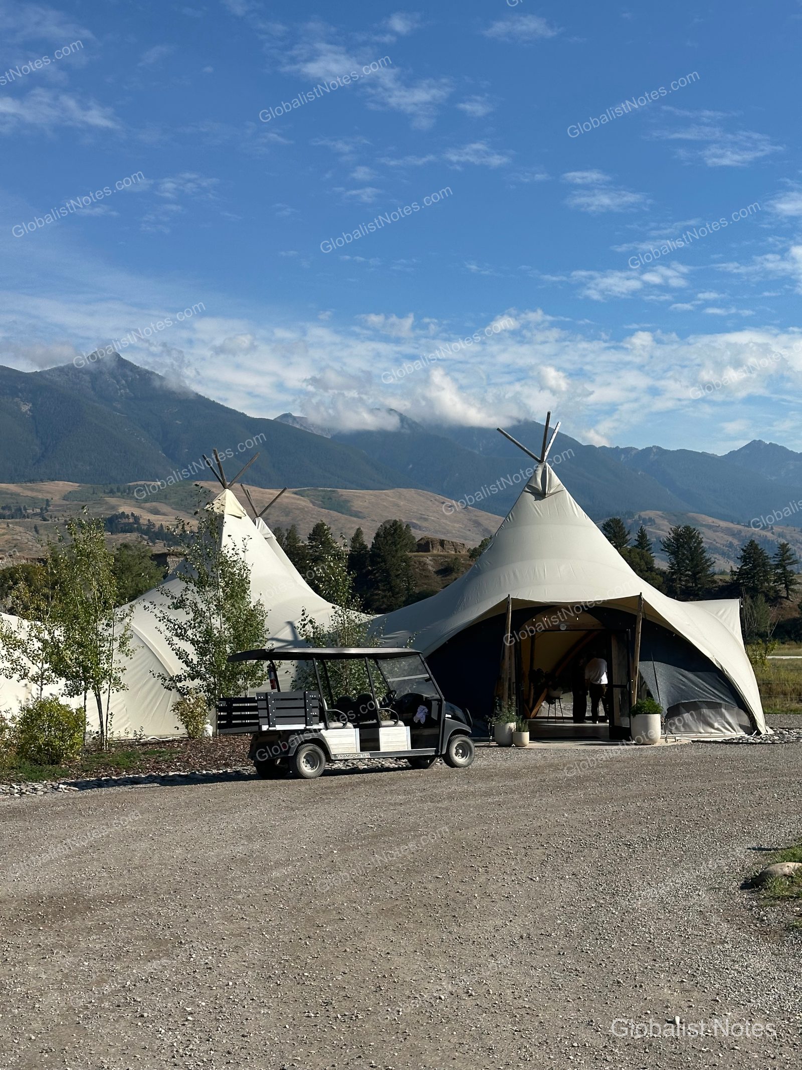 Under Canvas North Yellowstoneのテントと、その前に停められた黒いゴルフカート。背景には晴天の下、雄大な山脈が広がっています。