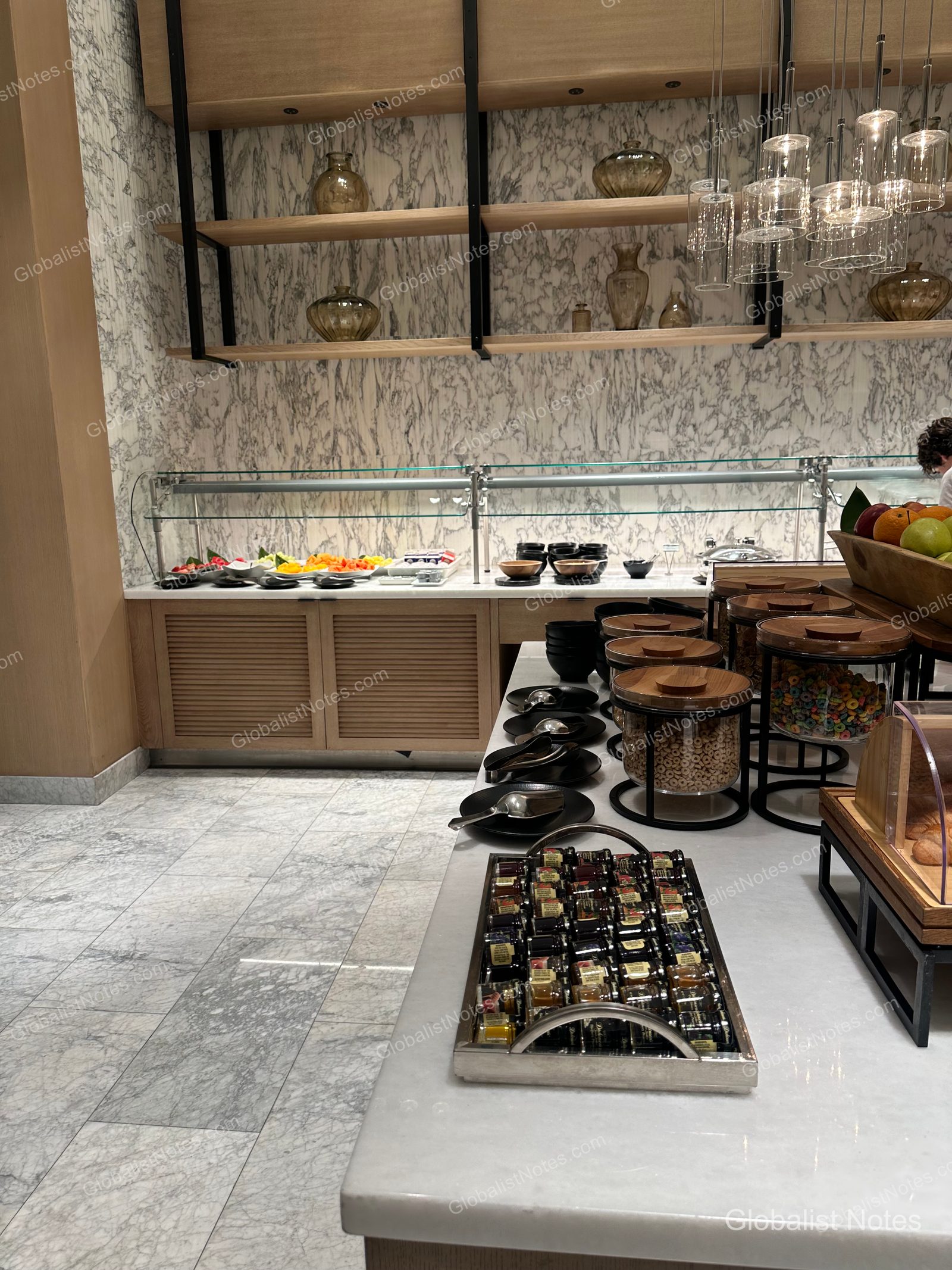 Hyatt Regency Newport Beach West 早餐自助餐區，大理石牆面與木製層架上整齊擺放著水果、麥片罐與果醬。