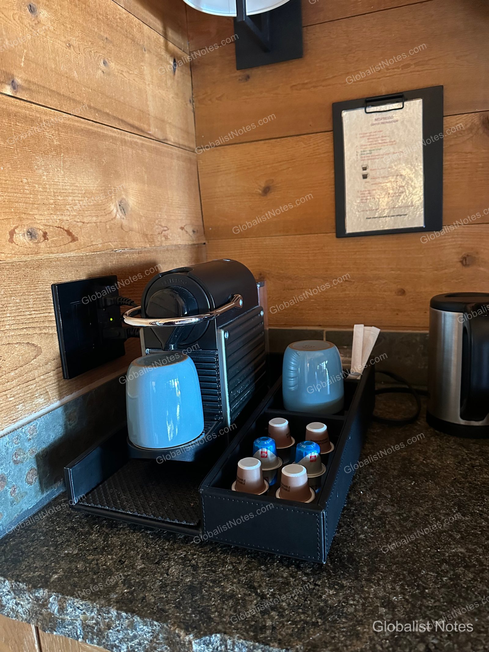 A Nespresso machine, capsules, and blue mugs on a dark tray against a wooden wall in an Alila Ventana Big Sur Junior Suite.