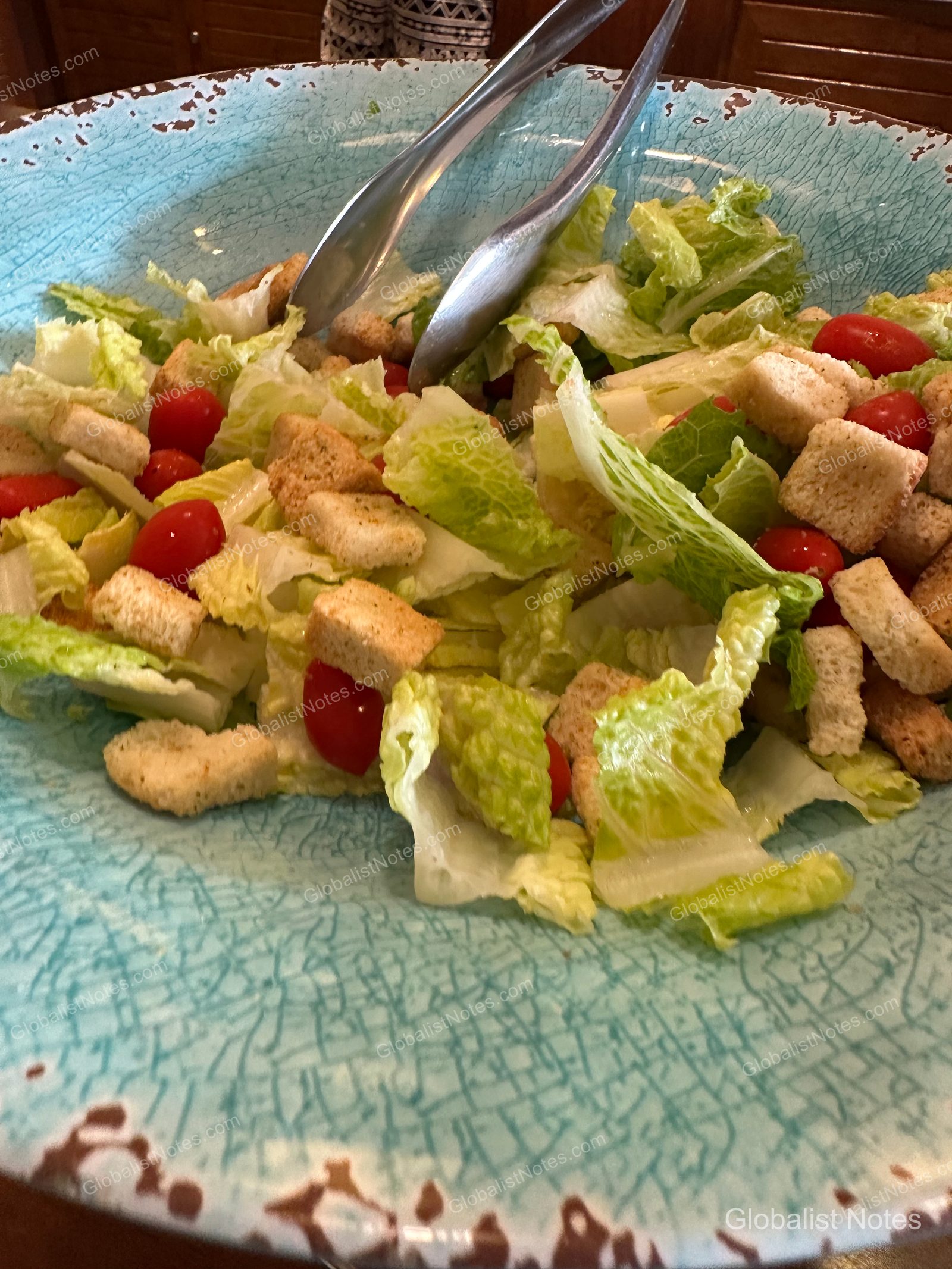 A salad served at a restaurant at Hyatt Regency Maui Resort and Spa in Lahaina, Hawaii. The salad, featuring romaine lettuce, cherry tomatoes, and croutons, is presented in a large, light blue bowl with a crackled pattern, with metal tongs resting inside.