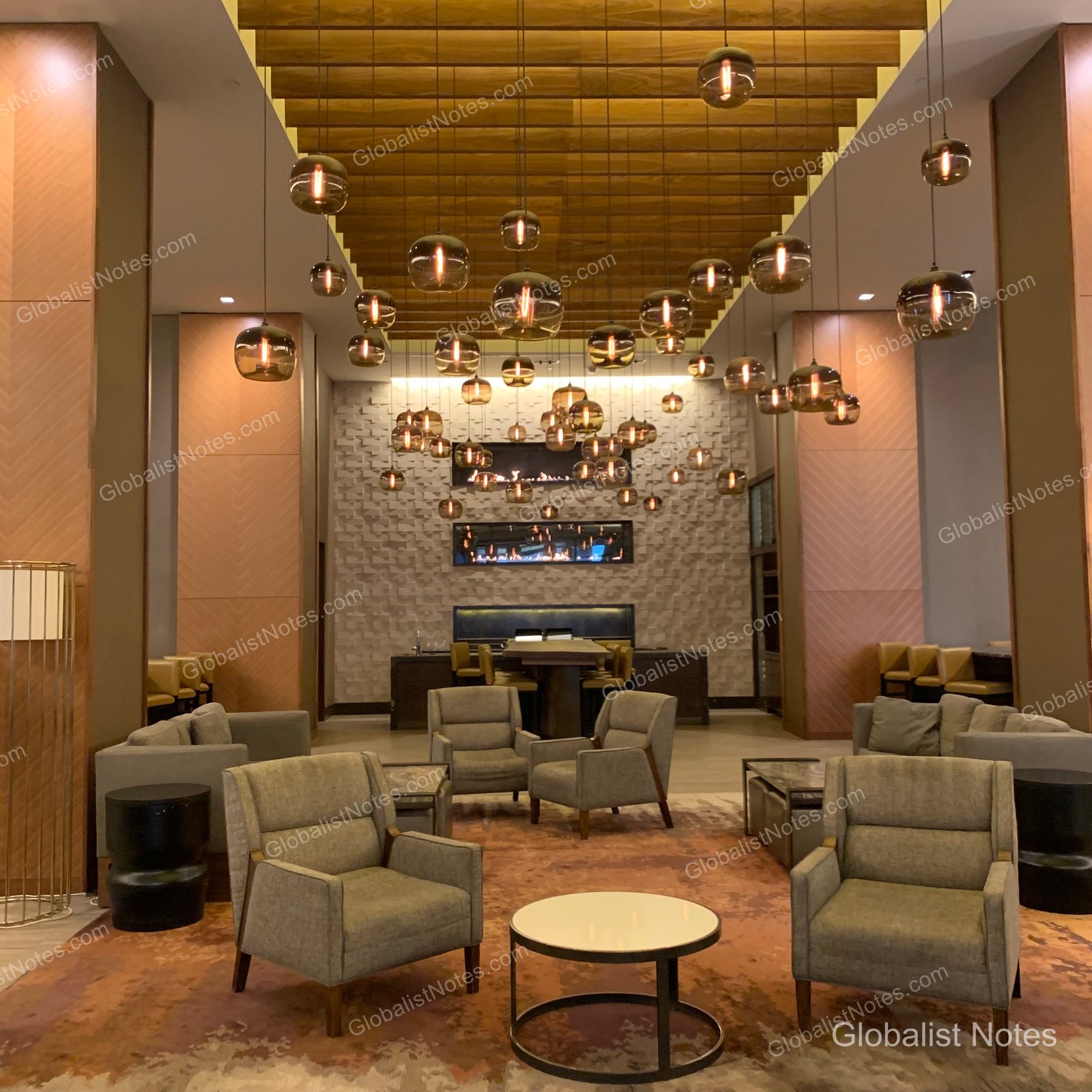 Grand Hyatt Denverのロビーラウンジ。天井から吊り下げられた多数の球体ペンダントライトと、グレーのアームチェア、ローテーブルが配置されている。壁面には暖炉があり、温かみのある落ち着いた雰囲気。