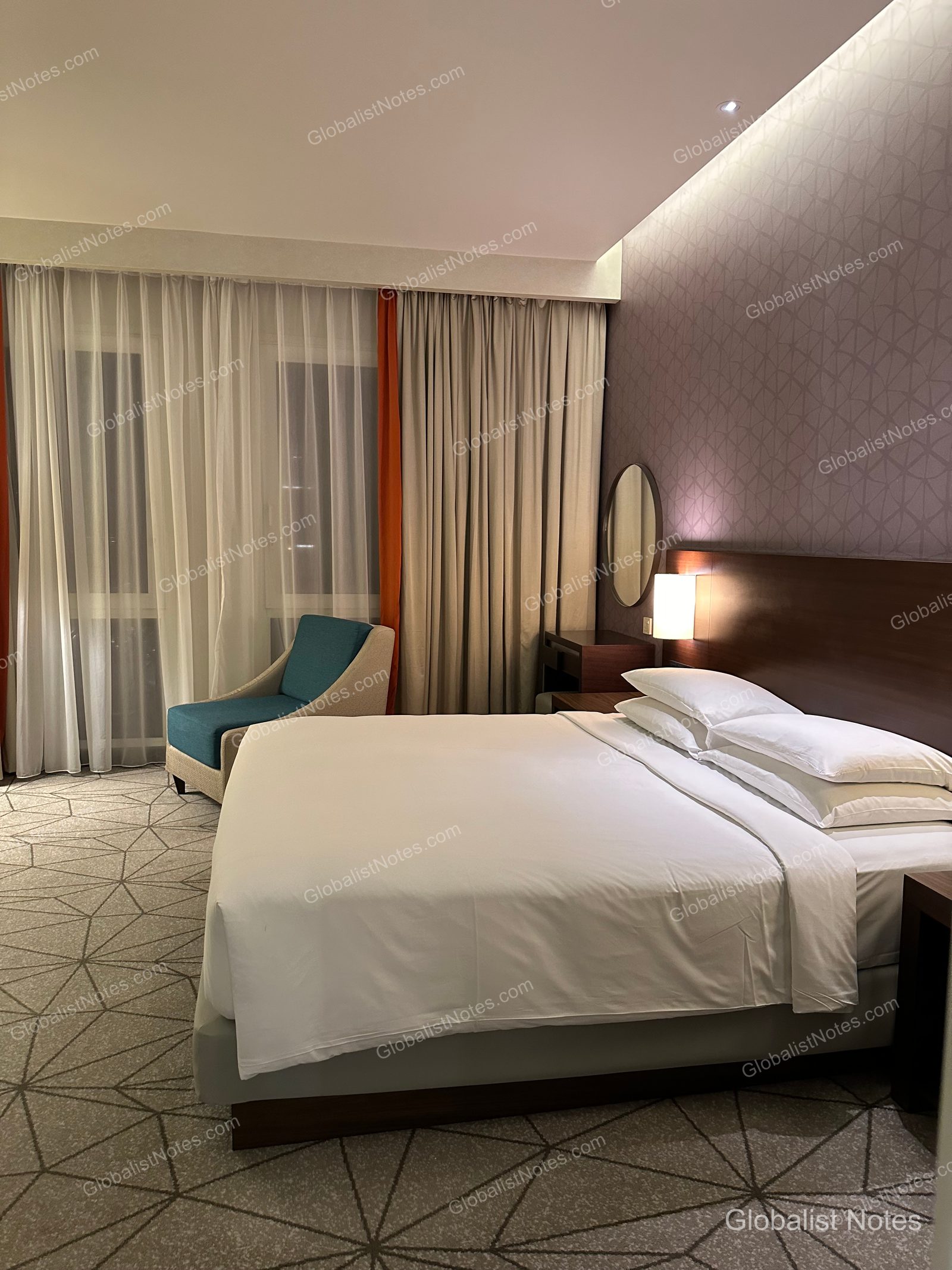 Hyatt Place Dubai Wasl District 一房套房臥室。King Size 床鋪旁設有靠窗的青綠色單人沙發，床頭板配有柔和燈光，地面鋪設幾何圖案地毯。