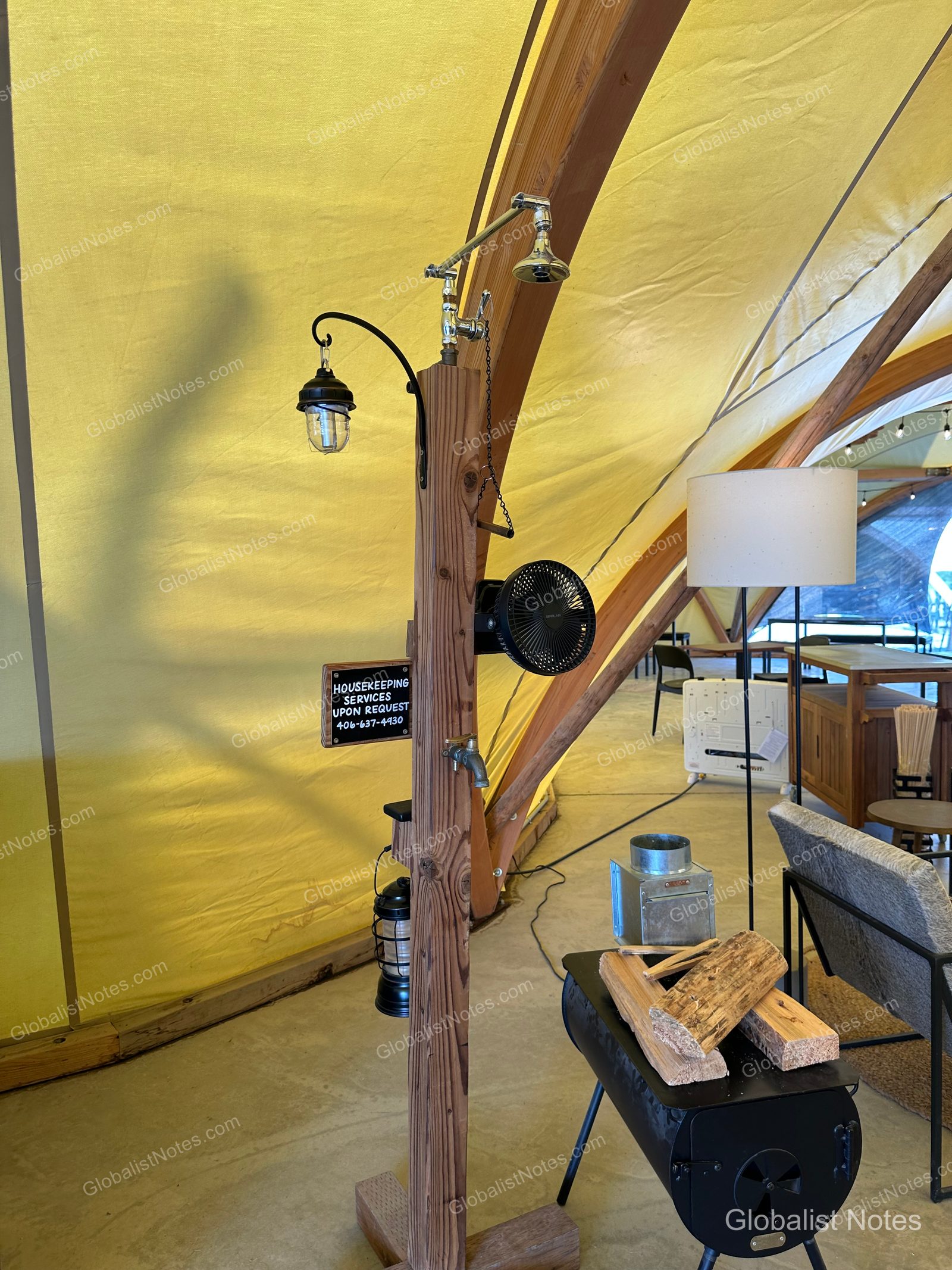Under Canvas North Yellowstoneのテント内部。木製の柱に備え付けられた照明と扇風機、ハウスキーピングの案内板、そして薪ストーブの様子。