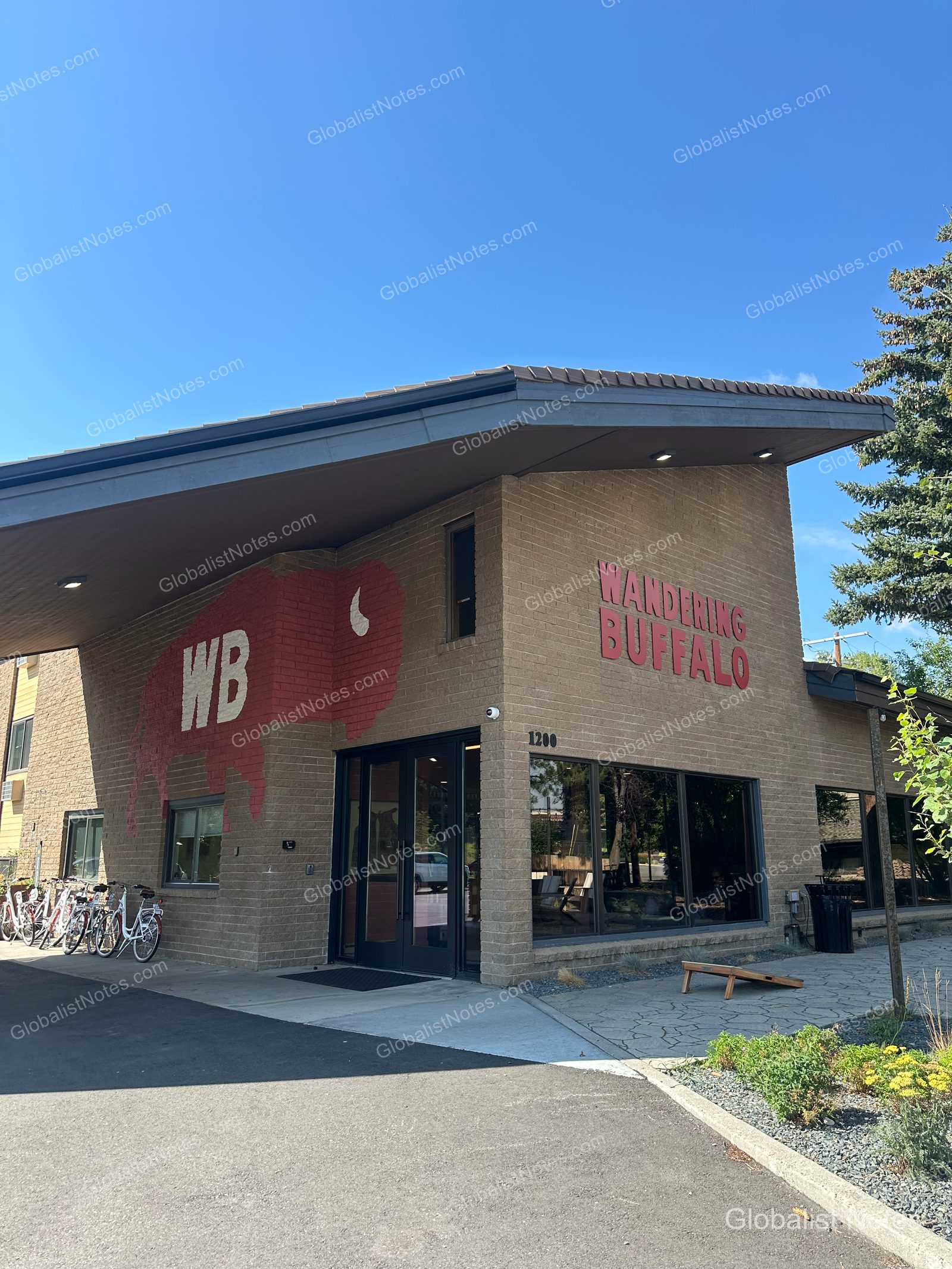 米国ボーズマンにあるWandering Buffaloの外観。茶色のレンガ壁に赤いバッファローのロゴと「WB」のイニシャルが描かれ、建物の前には貸出用の自転車が並んでいます。