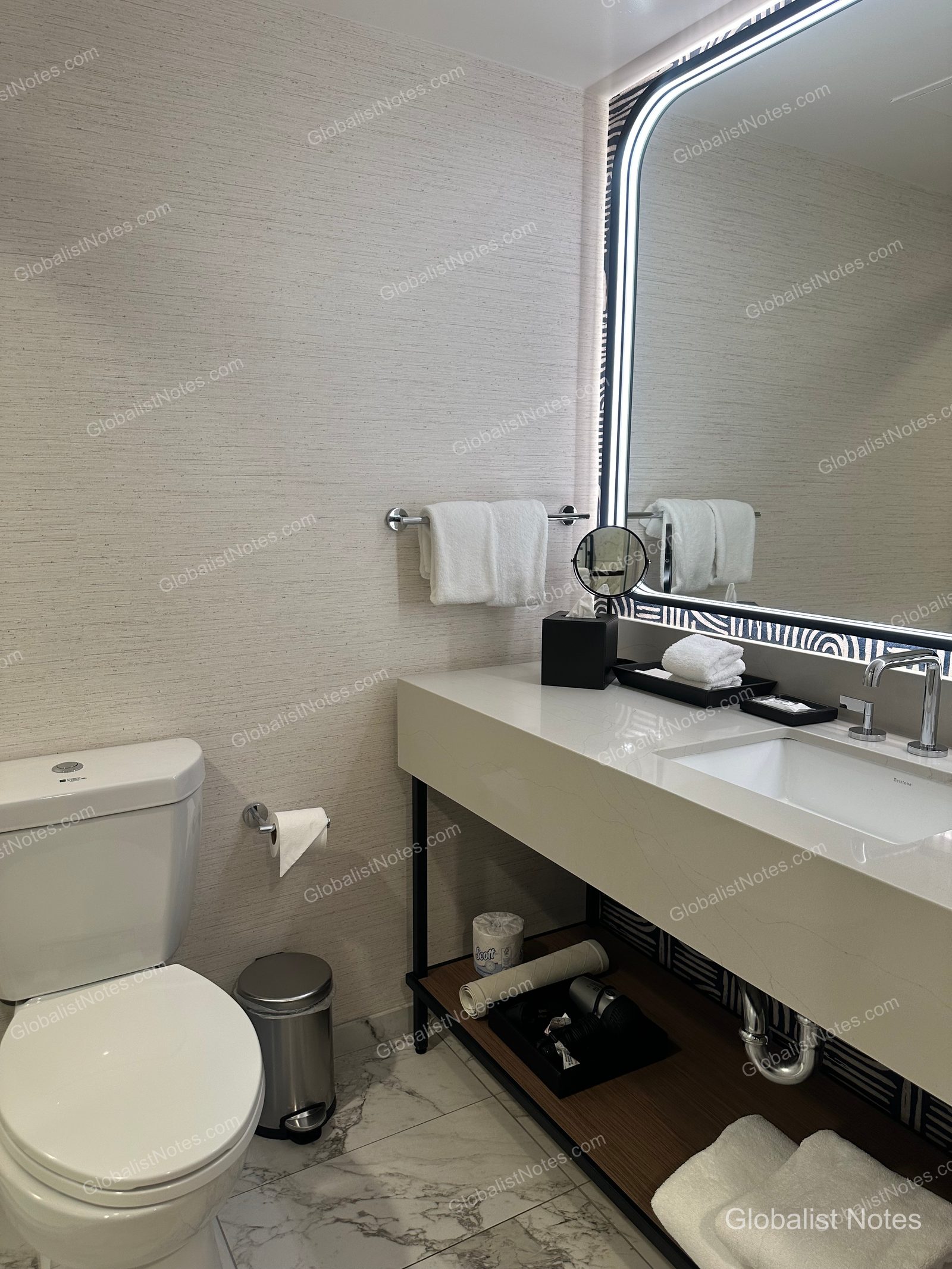 Hyatt Regency Irvine One-Bedroom Suite 浴室內部，採用明亮色調壁紙與大理石地板，配備帶 LED 背光的鏡面洗手台與馬桶，空間整潔明亮。