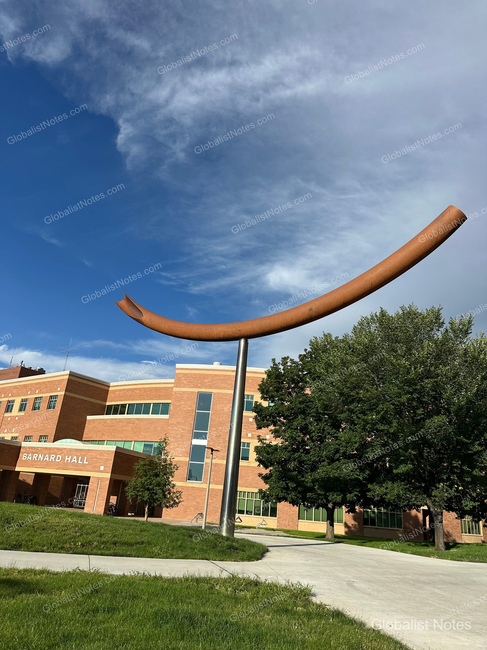 ベルグレードにあるBarnard Hallの建物前。青空を背景に、巨大な曲線を描く錆びた金属製の彫刻が設置され、周囲には木々や芝生が広がっています。