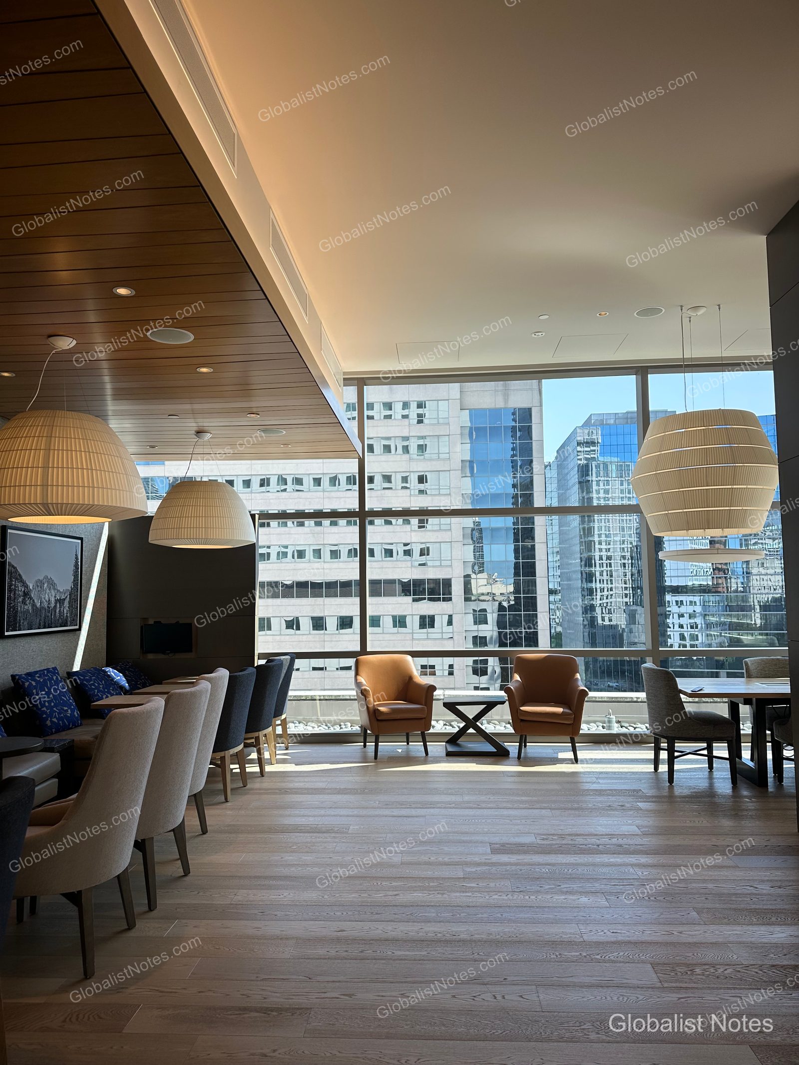 Interior of the Hyatt Regency Seattle lounge, featuring high ceilings and floor-to-ceiling windows with views of the downtown Seattle skyline. The space has light wood flooring, modern pendant lighting, and a variety of seating arrangements, creating an open and calm atmosphere.