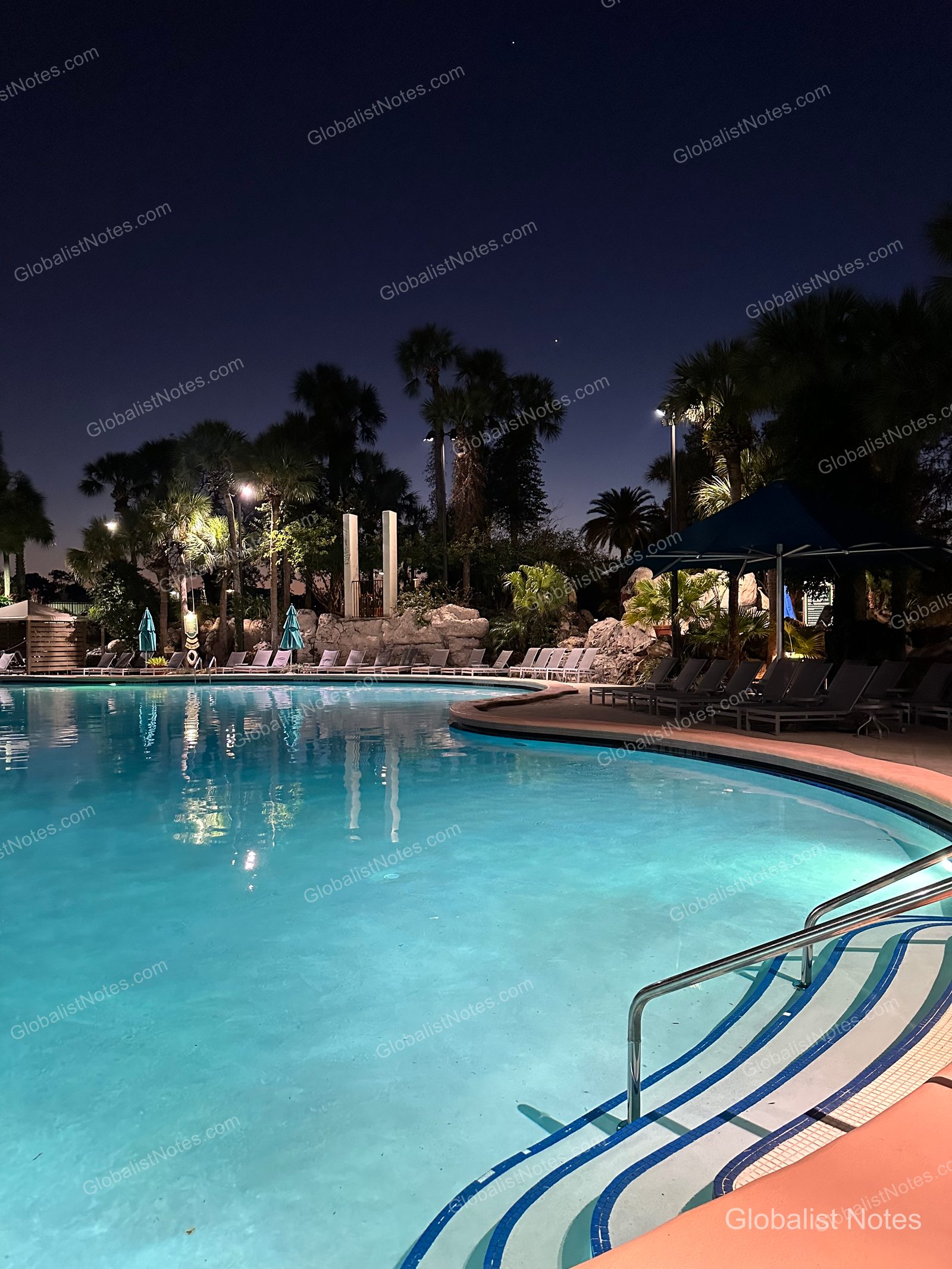 Night view of the outdoor pool at Hyatt Regency Grand Cypress, showing the illuminated curved pool, surrounding palm trees, and rows of sun loungers under the dark sky.