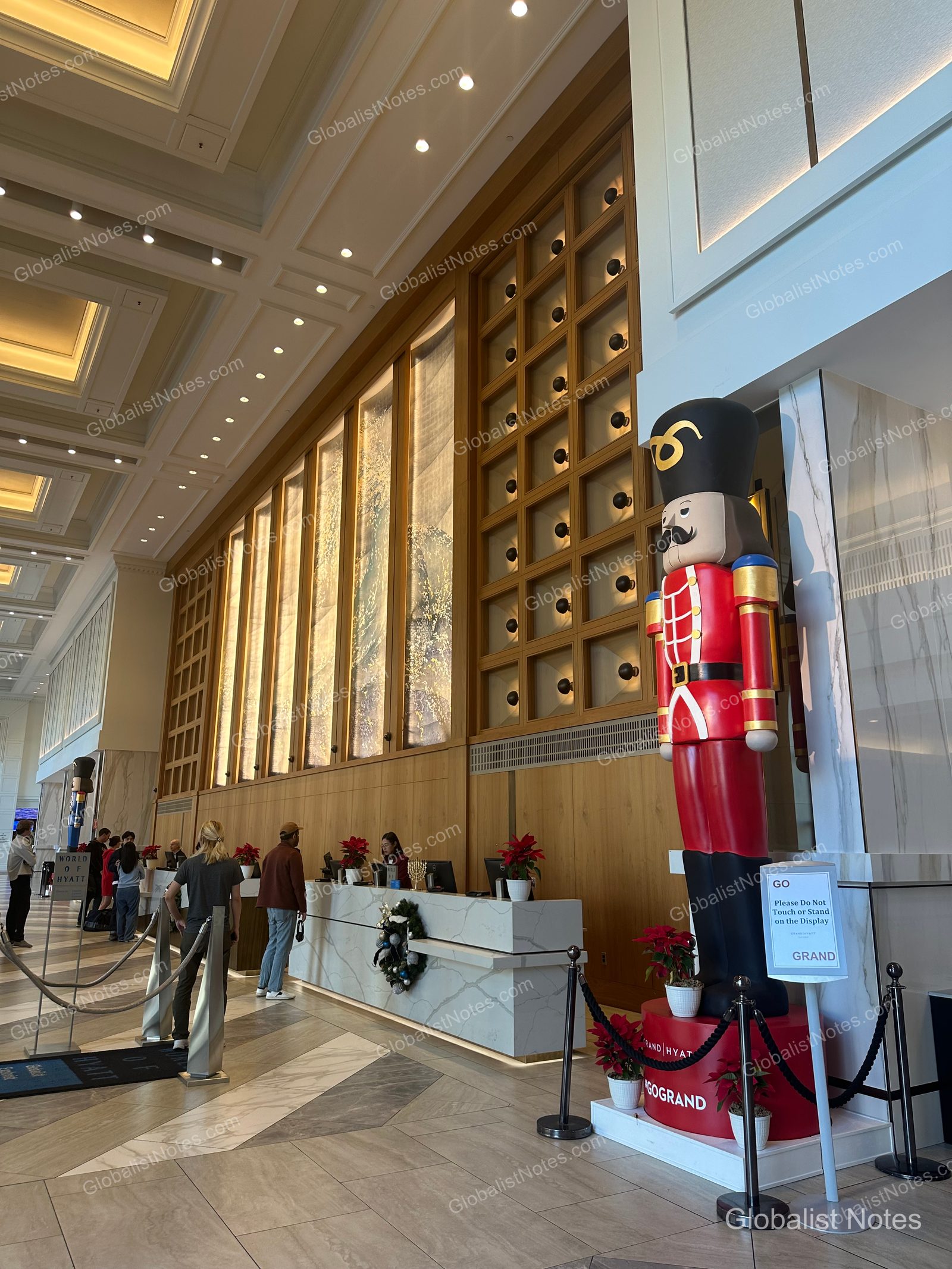 Manchester Grand Hyatt San Diego 大廳全景，挑高天花板與大理石牆面相當醒目。辦理入住櫃檯前擺放著聖誕裝飾，包括穿著紅色制服的大型胡桃鉗人偶，現場有住客正在排隊辦理入住。