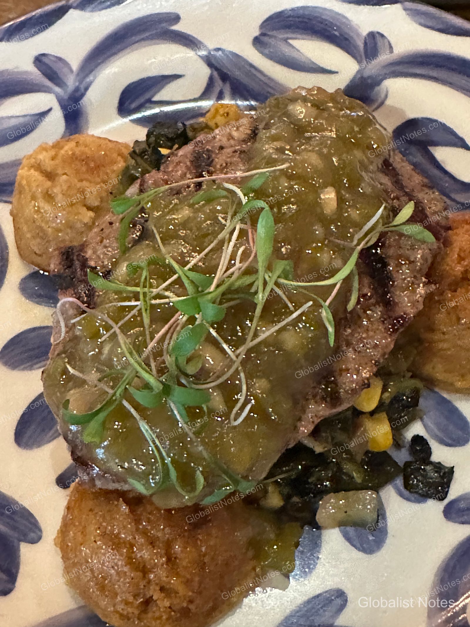 미라발 오스틴 리조트 앤 스파의 저녁 식사로, 그릴 자국이 남은 스테이크 위에 초록색 살사 소스와 새싹 채소를 올리고 옥수수와 곁들임 요리를 함께 담아낸 푸른색 꽃무늬 패턴 접시의 근접 촬영 모습입니다.
