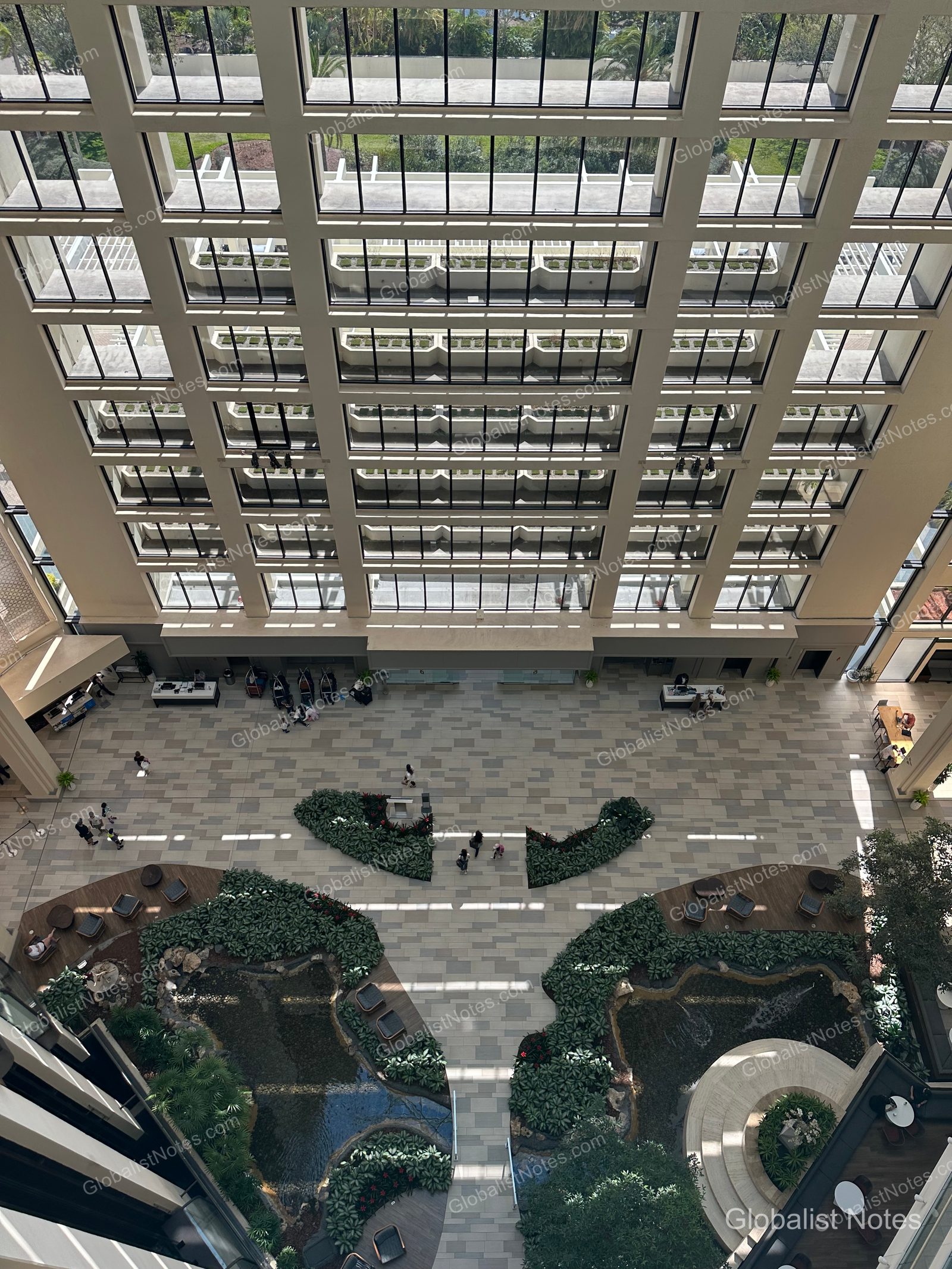A view of the massive atrium lobby at Hyatt Regency Grand Cypress in Orlando from a high floor, showing the grid-patterned glass ceiling, vertical guest room corridors, and the indoor garden and pond on the ground floor.