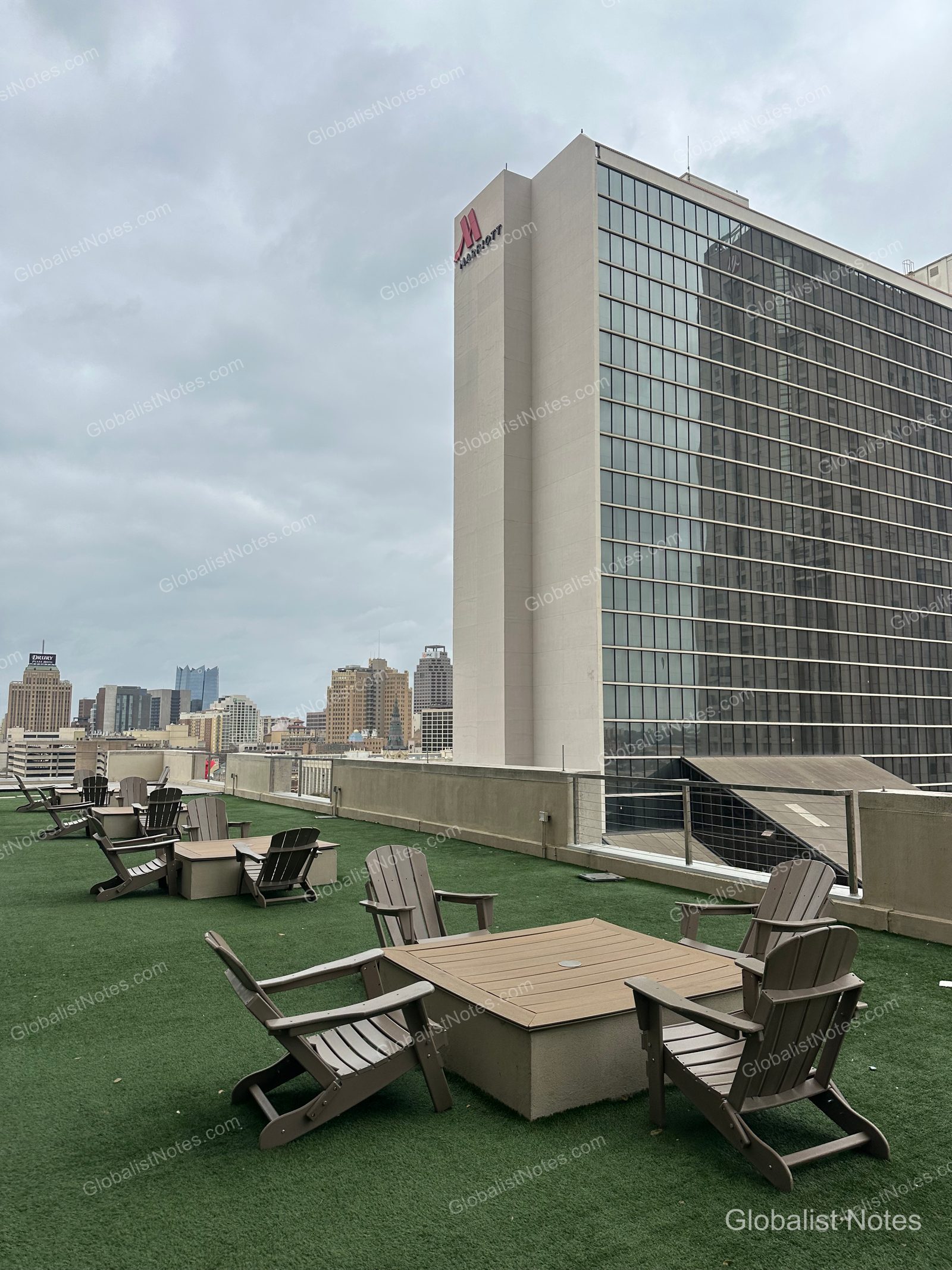 View of the rooftop terrace at Grand Hyatt San Antonio River Walk, featuring artificial turf, several wooden chairs and tables, and a backdrop of surrounding city buildings.
