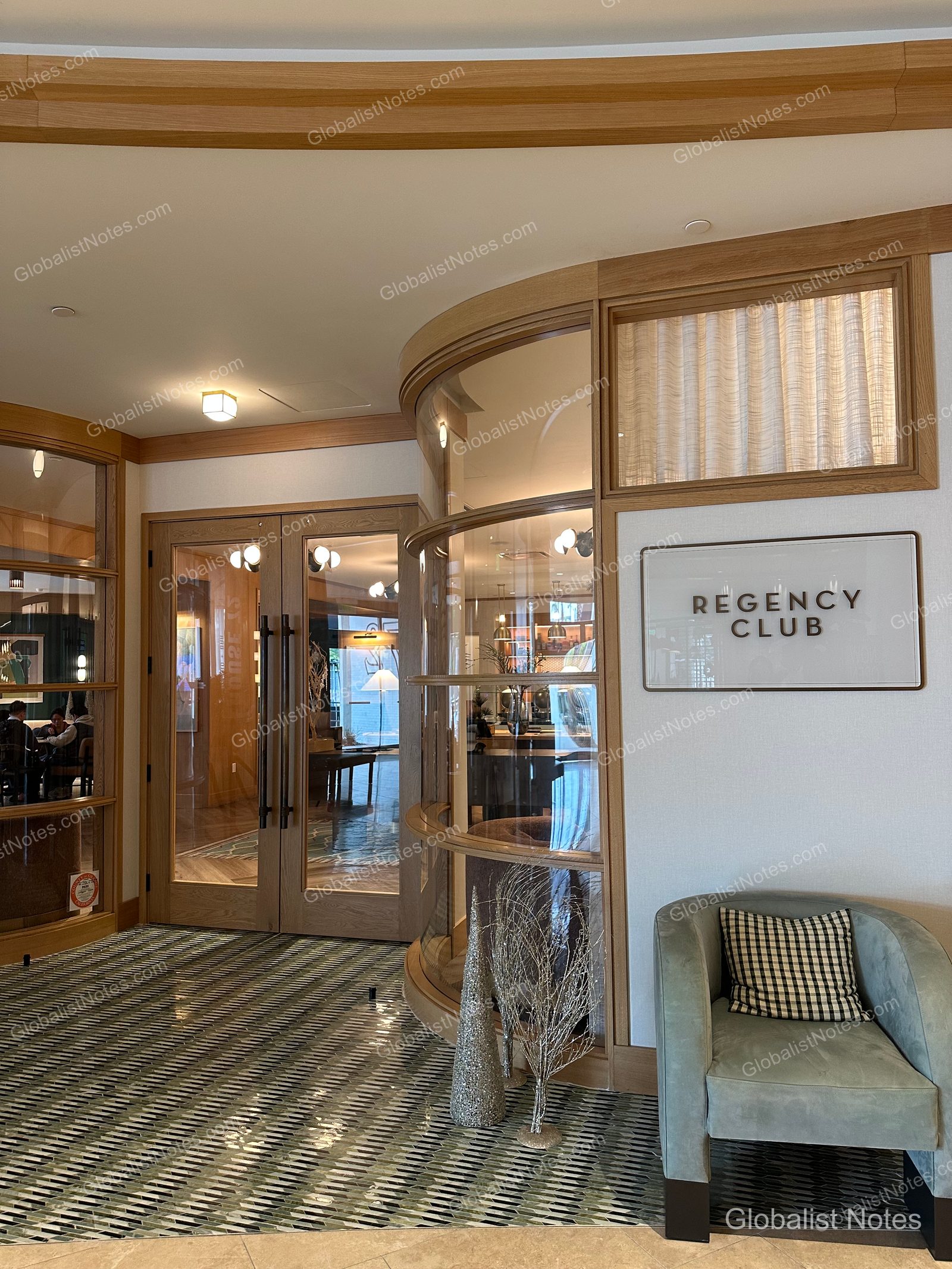 Hyatt Regency Irvine 的 Regency Club 入口，設有弧形玻璃牆與木框雙開門，側邊牆面掛有 Regency Club 標示，並擺放一張配有格紋靠墊的單人沙發。