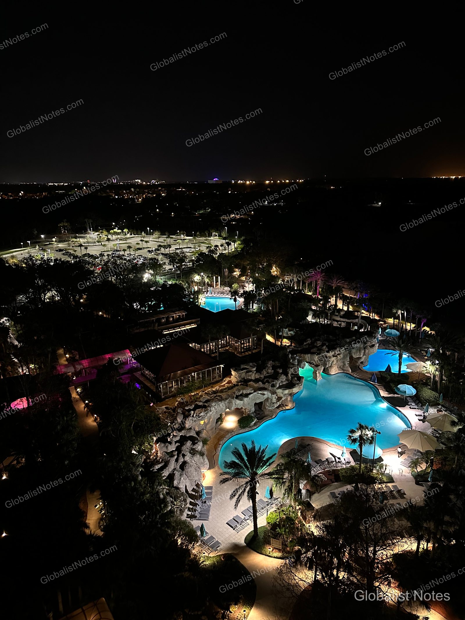 A night view from a guest room at Hyatt Regency Grand Cypress, overlooking the illuminated large swimming pool, rock formations, palm trees, and distant city lights.