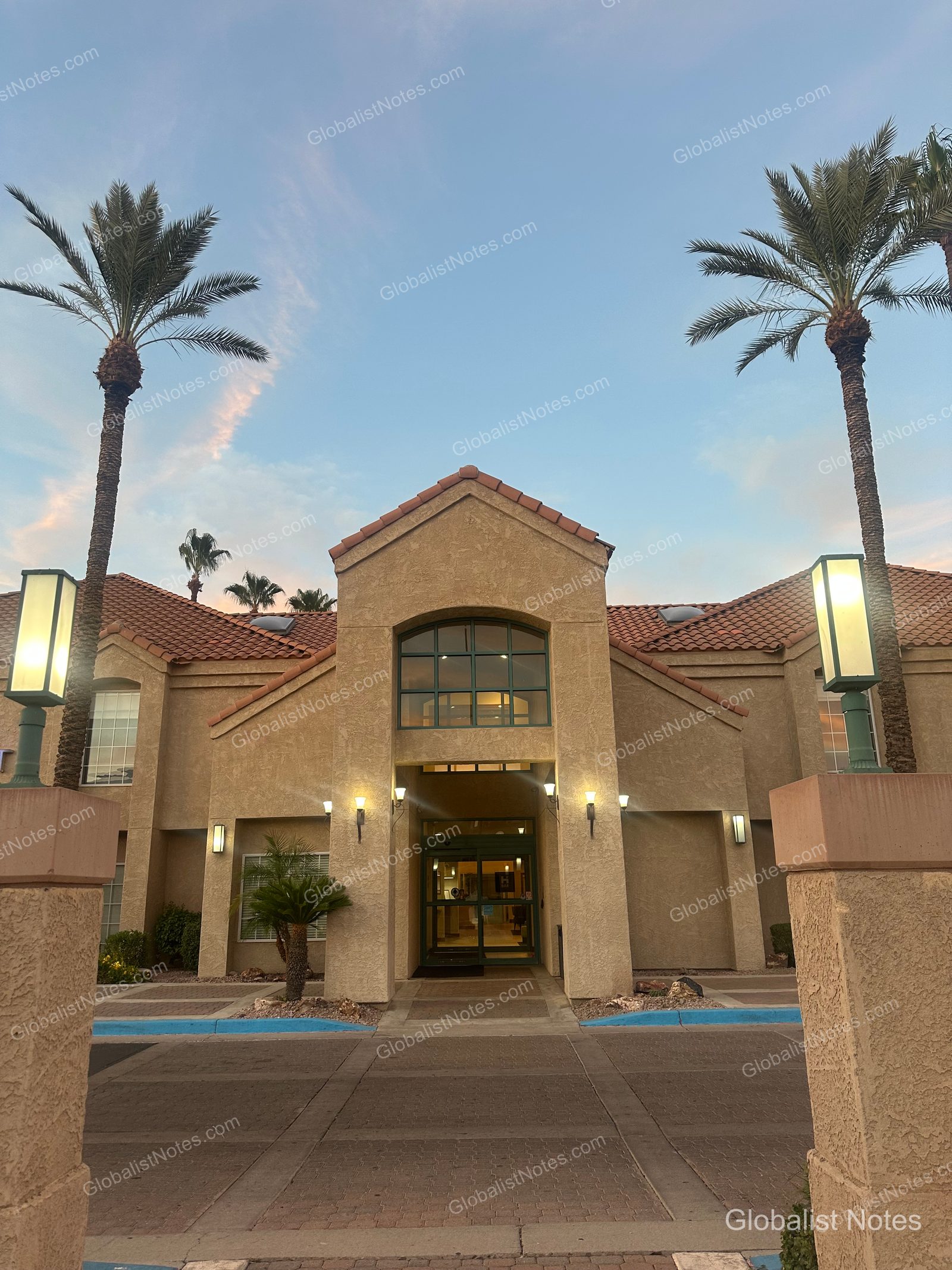 夕暮れ時のHyatt House Scottsdale/Old Townの外観。黄土色の壁と赤い瓦屋根が特徴的で、入口の両脇にはヤシの木が並んでいます。