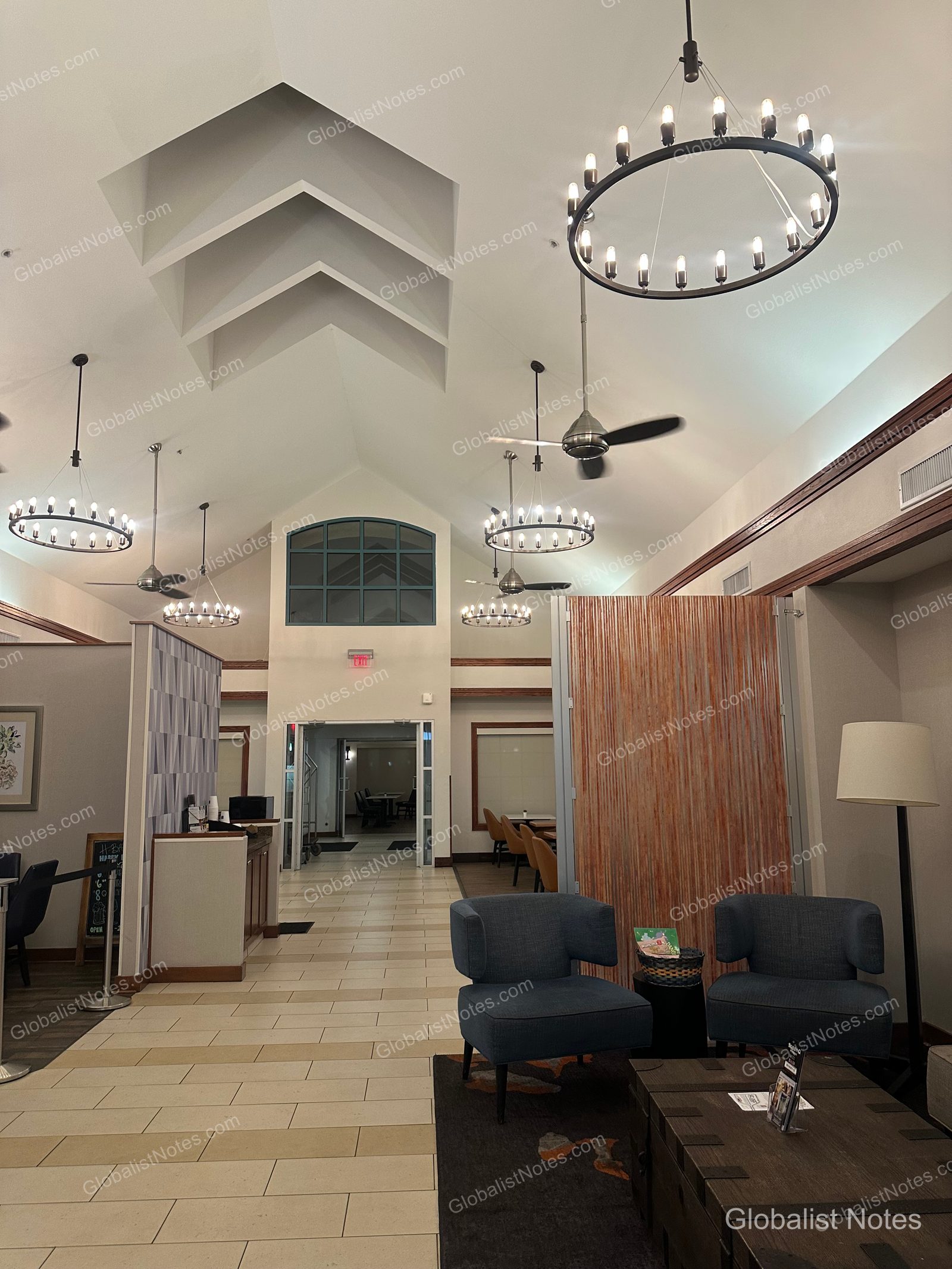 高い切妻屋根の天井に丸いシャンデリアが吊り下げられたHyatt House Scottsdale/Old Townのロビー。青い一人掛けソファと木製テーブルが配置されている。