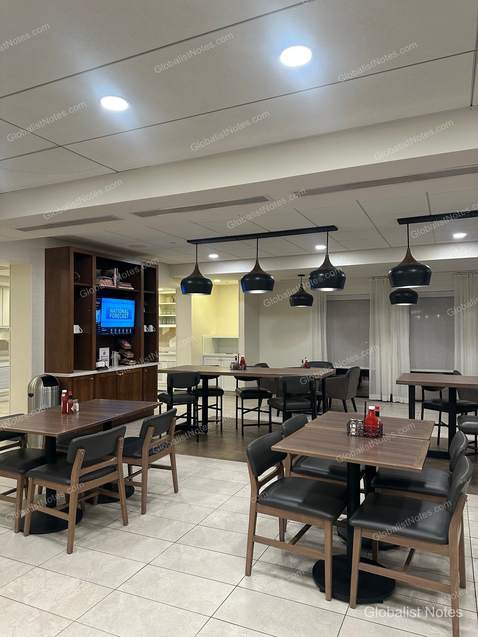 Hyatt Place Tucson Central 早餐區，擺放多張方形餐桌與黑色皮椅。天花板裝有吊燈，牆面設有嵌入電視的木質收納櫃。
