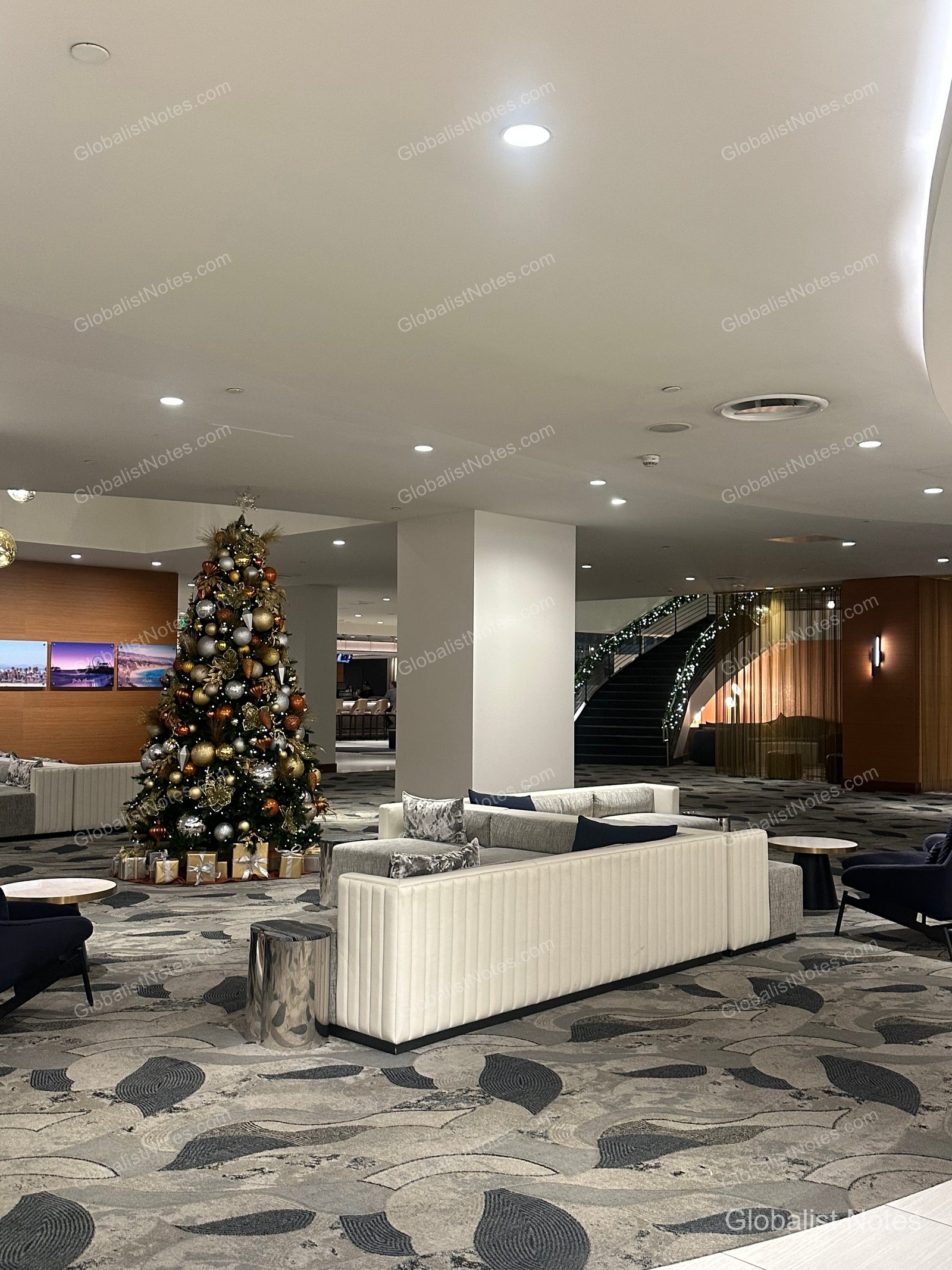 Lobby view of Hyatt Regency Los Angeles International Airport. A large, ornate Christmas tree stands in the center, with a spacious seating area featuring modern white sofas and a uniquely patterned curved carpet.
