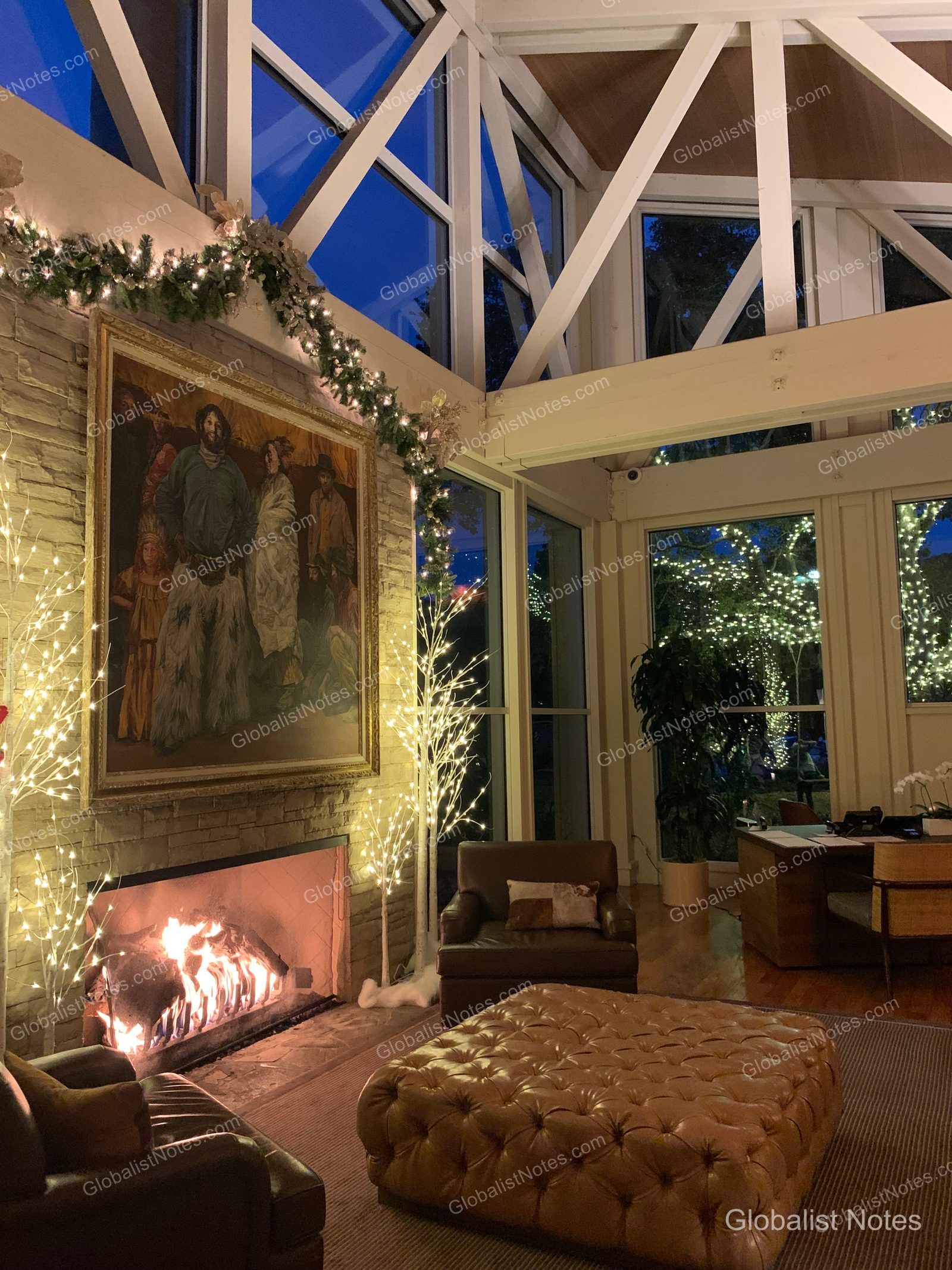 カーメル・バレー・ランチのロビー。高い天井と大きな窓の向こうにクリスマスイルミネーションが輝く夜の風景。暖炉には火が灯り、その上には大きな油絵が飾られ、周囲はクリスマス装飾で彩られている。