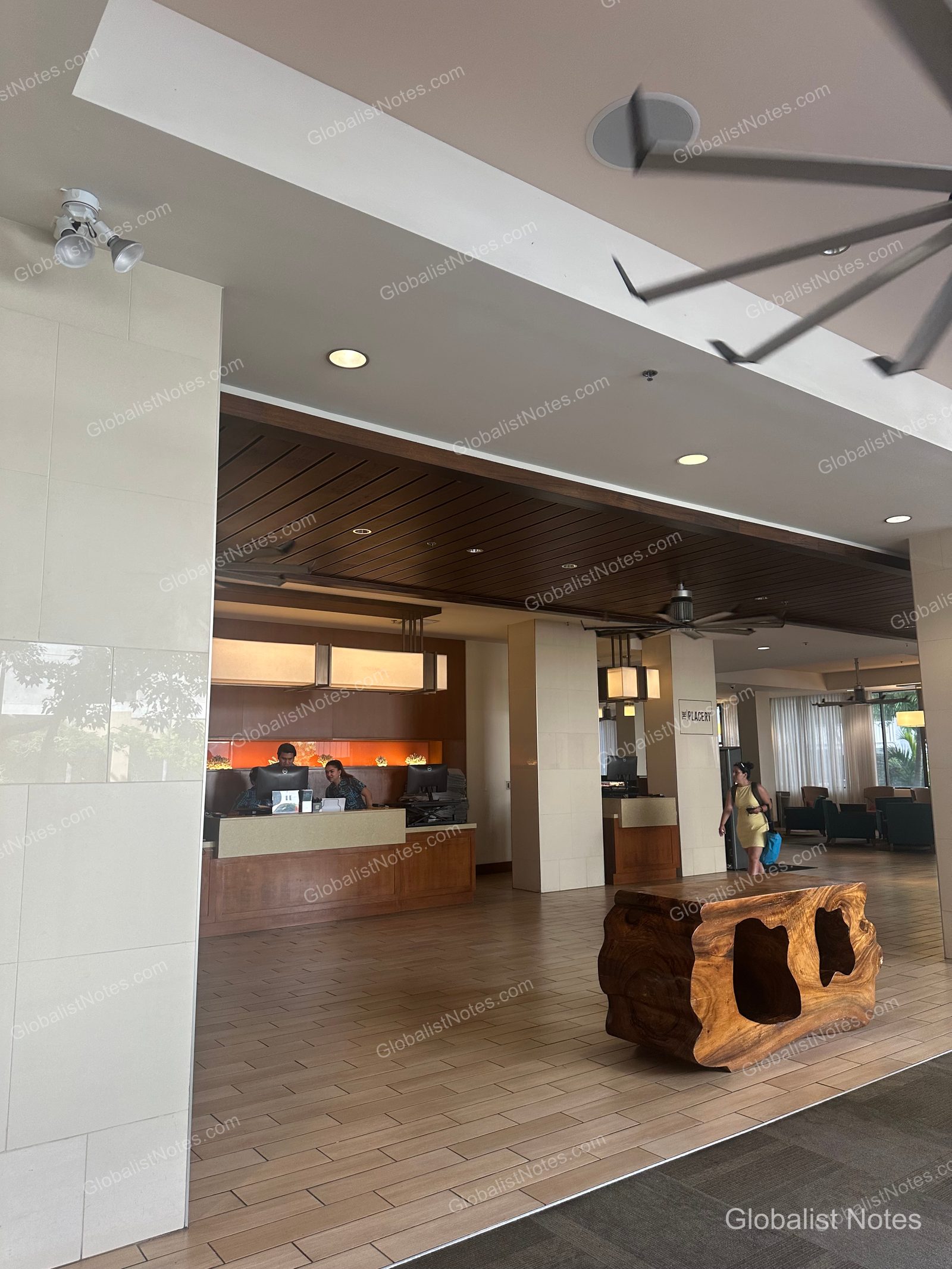 Lobby of Hyatt Place Waikiki Beach in Honolulu, Hawaii. A uniquely shaped wooden bench sits in the center, with the check-in desk and 'The Placery' signage visible in the background.